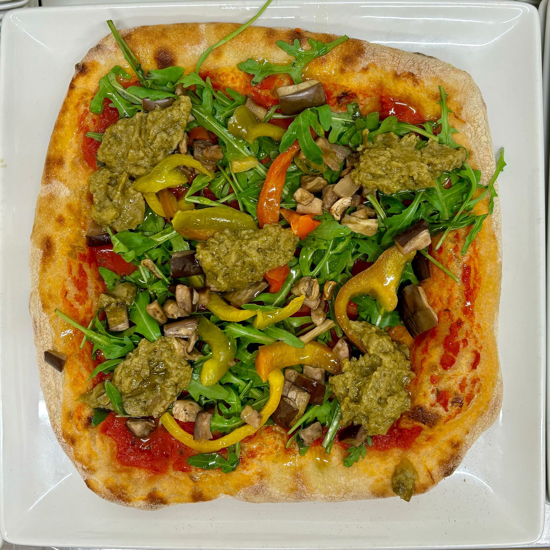 Una pizza con tante verdure sopra su un piatto bianco