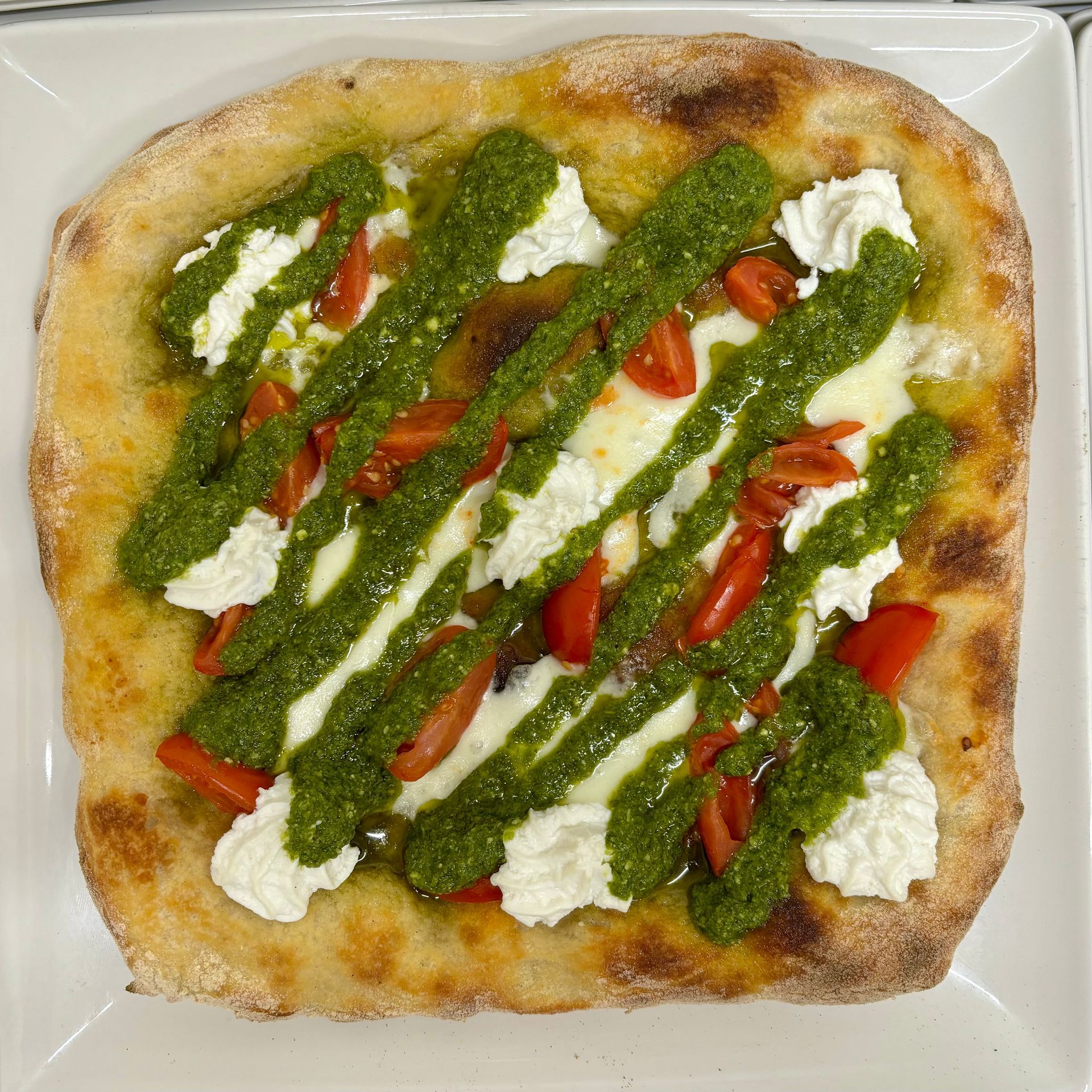 Una pizza con pesto e pomodori su un piatto bianco