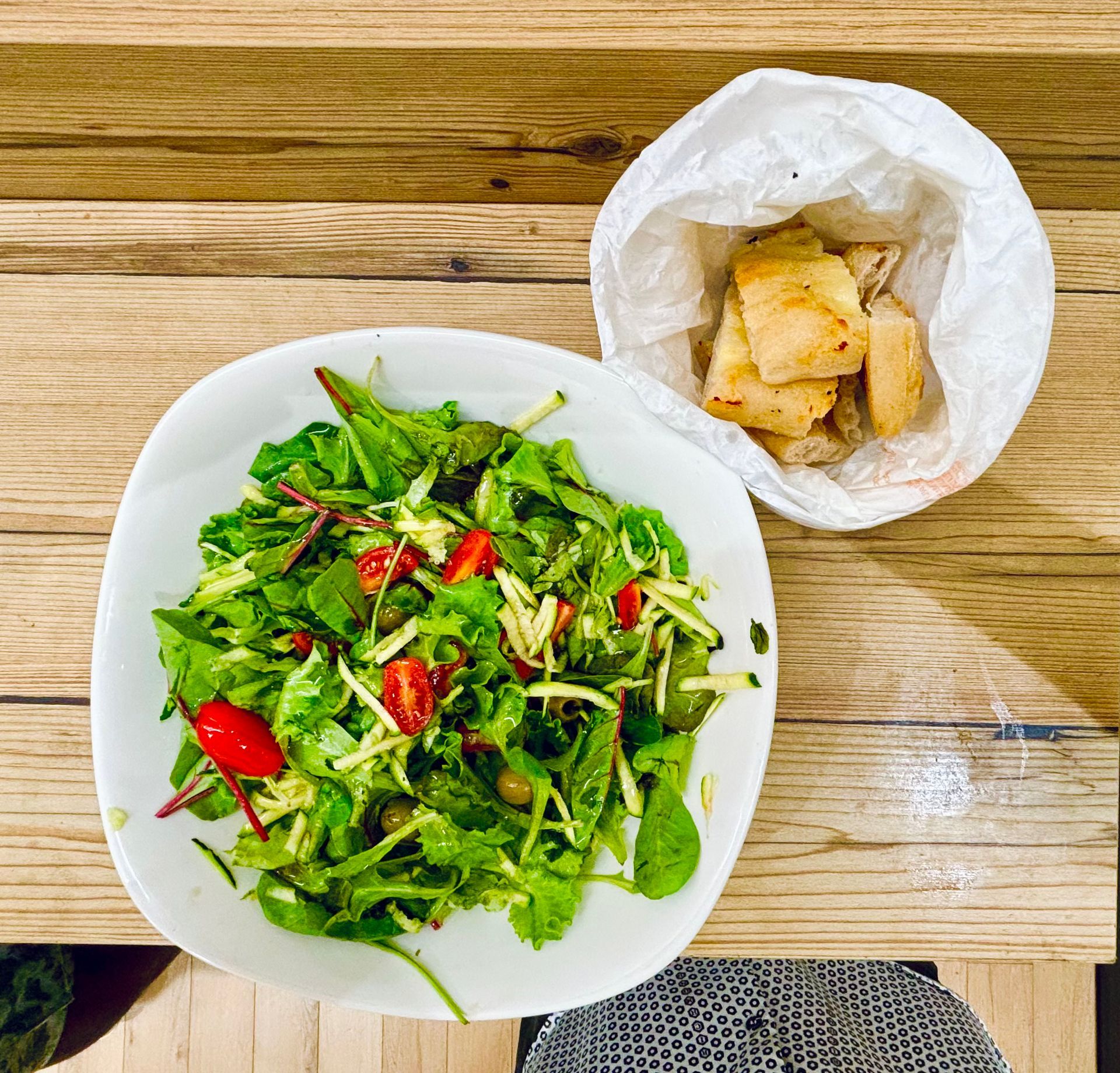 Una ciotola di insalata accanto a una ciotola di pane su un tavolo di legno
