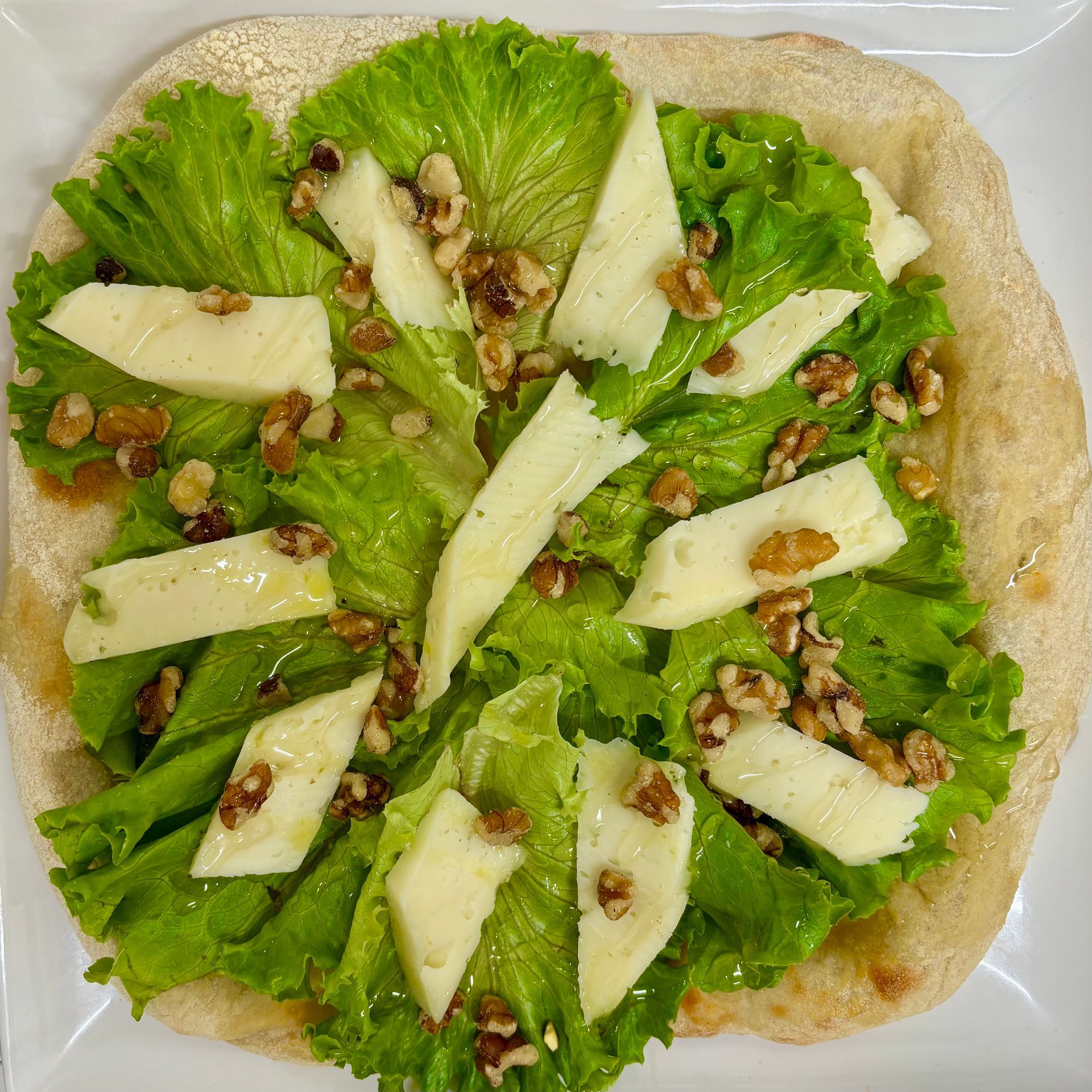 Una pizza con lattuga, formaggio e noci su un piatto bianco.