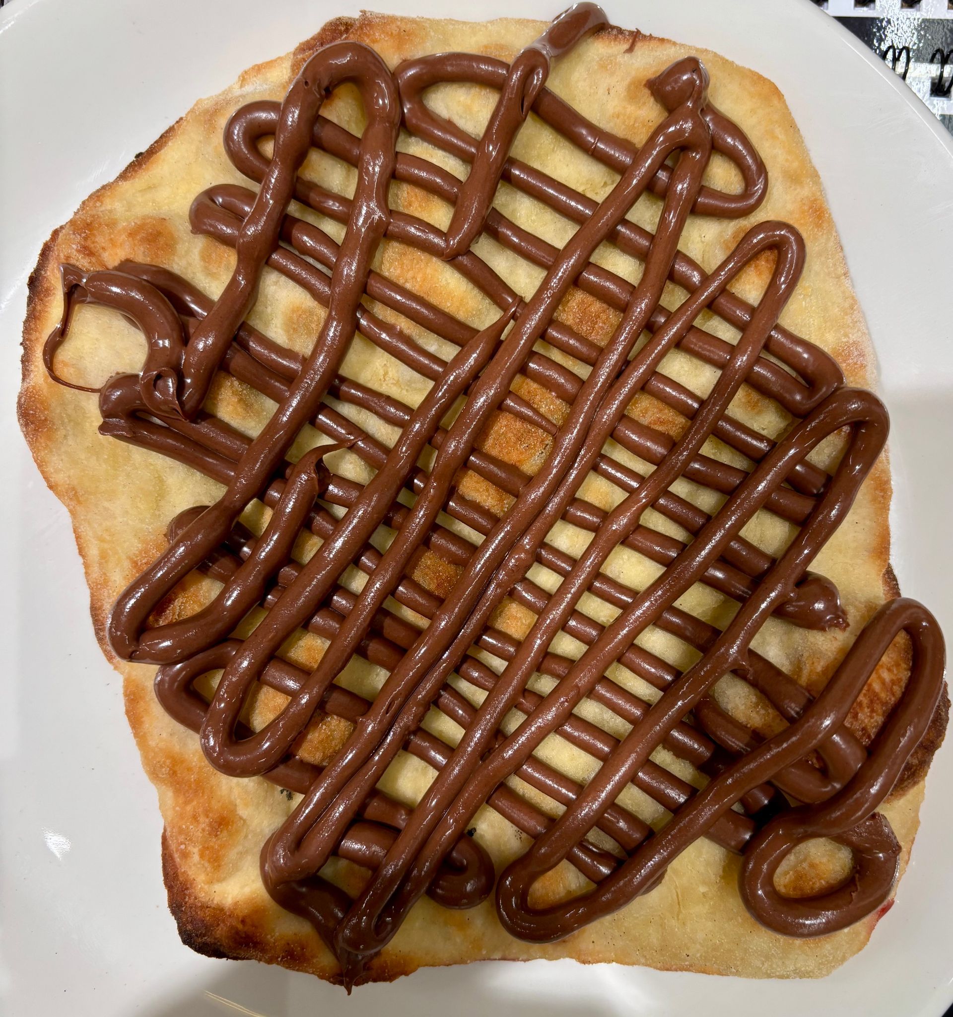 Un pezzo di pizza con salsa al cioccolato sopra su un piatto bianco.