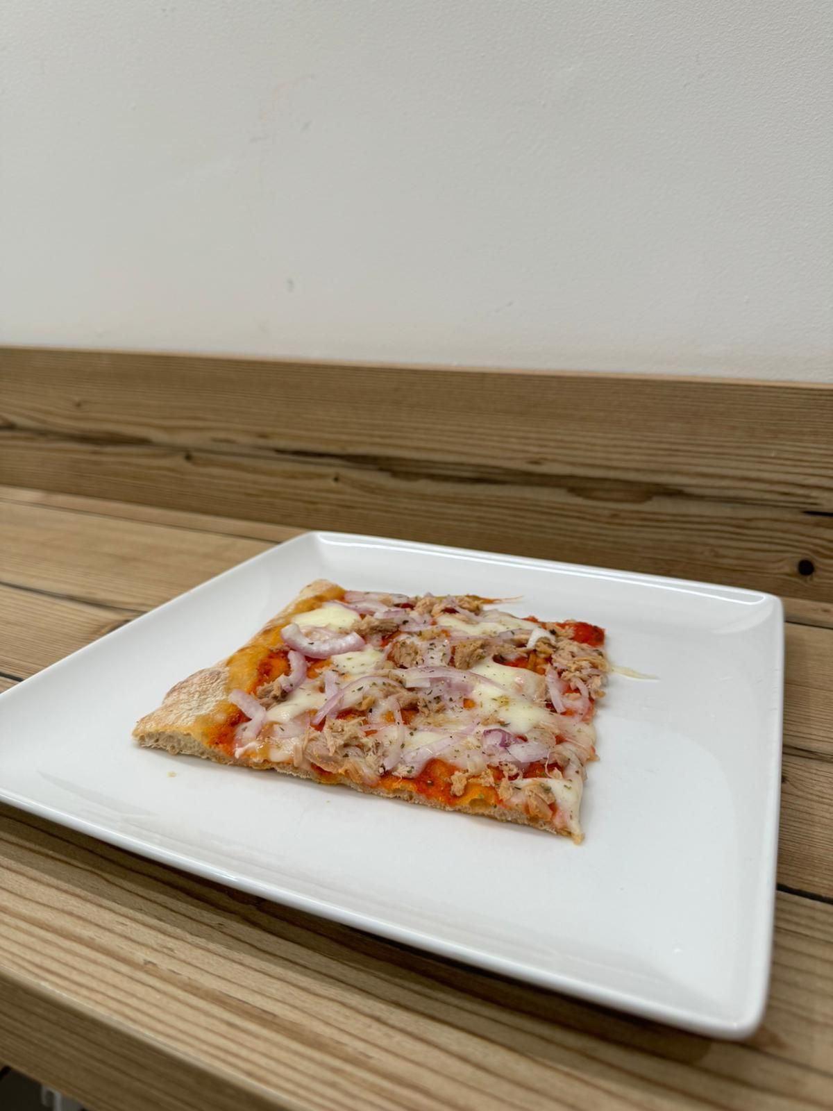 Una fetta di pizza è su un piatto bianco su un tavolo di legno.