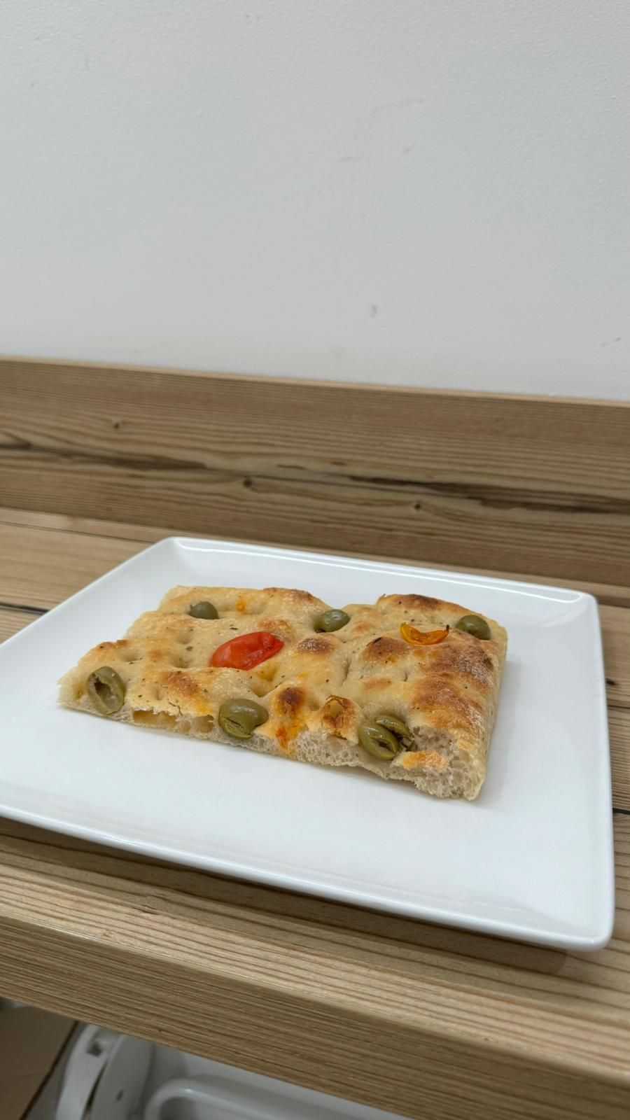 Una fetta di pizza con olive e pomodori su un piatto bianco su un tavolo di legno.