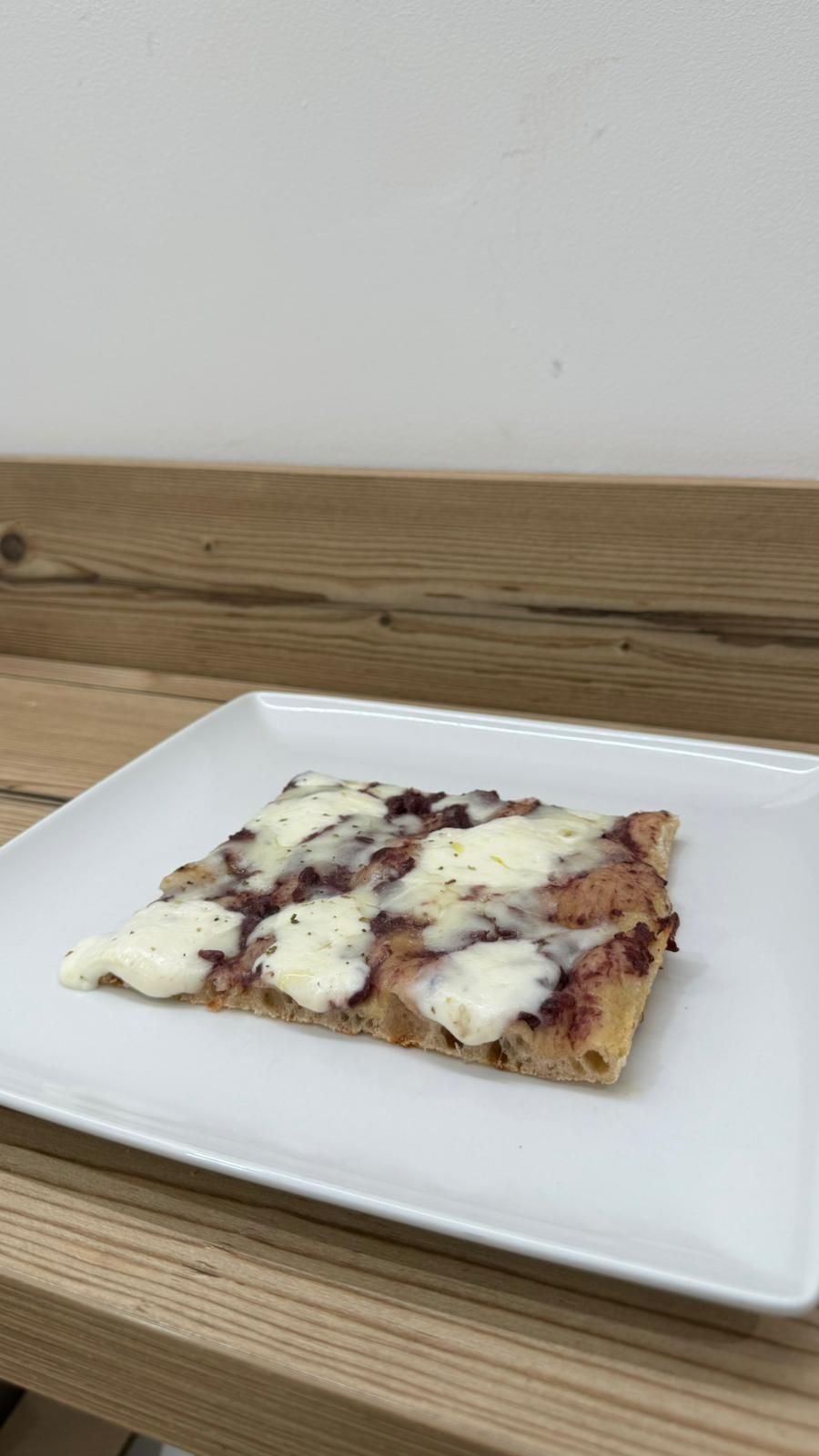 Una fetta di pizza è su un piatto bianco su un tavolo di legno.