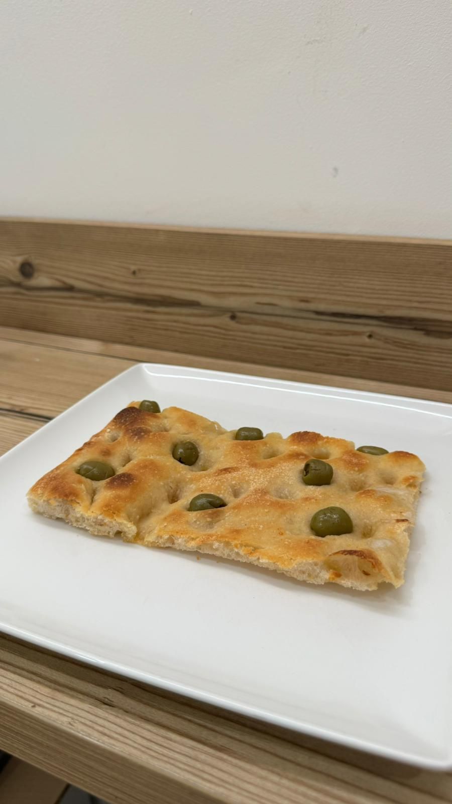 Una fetta di pizza con le olive su un piatto bianco su un tavolo di legno.