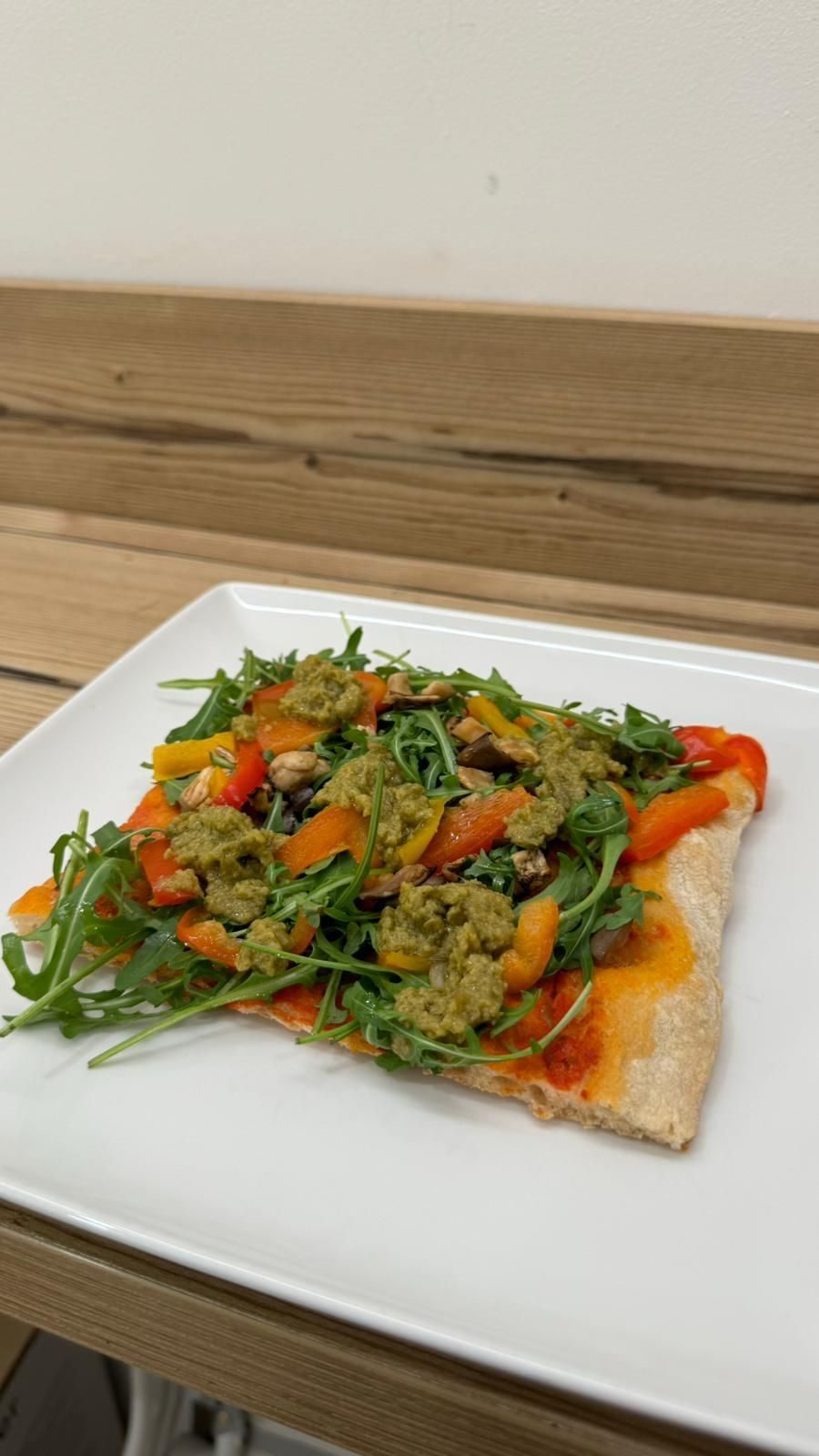 Una fetta di pizza con verdure su un piatto bianco su un tavolo di legno.