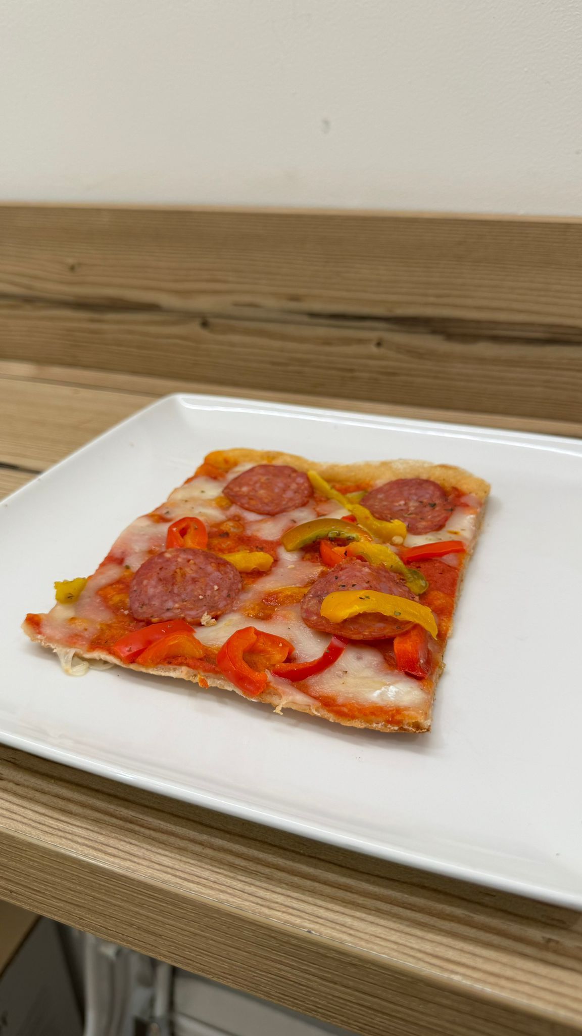 Una fetta di pizza è su un piatto bianco su un tavolo di legno.