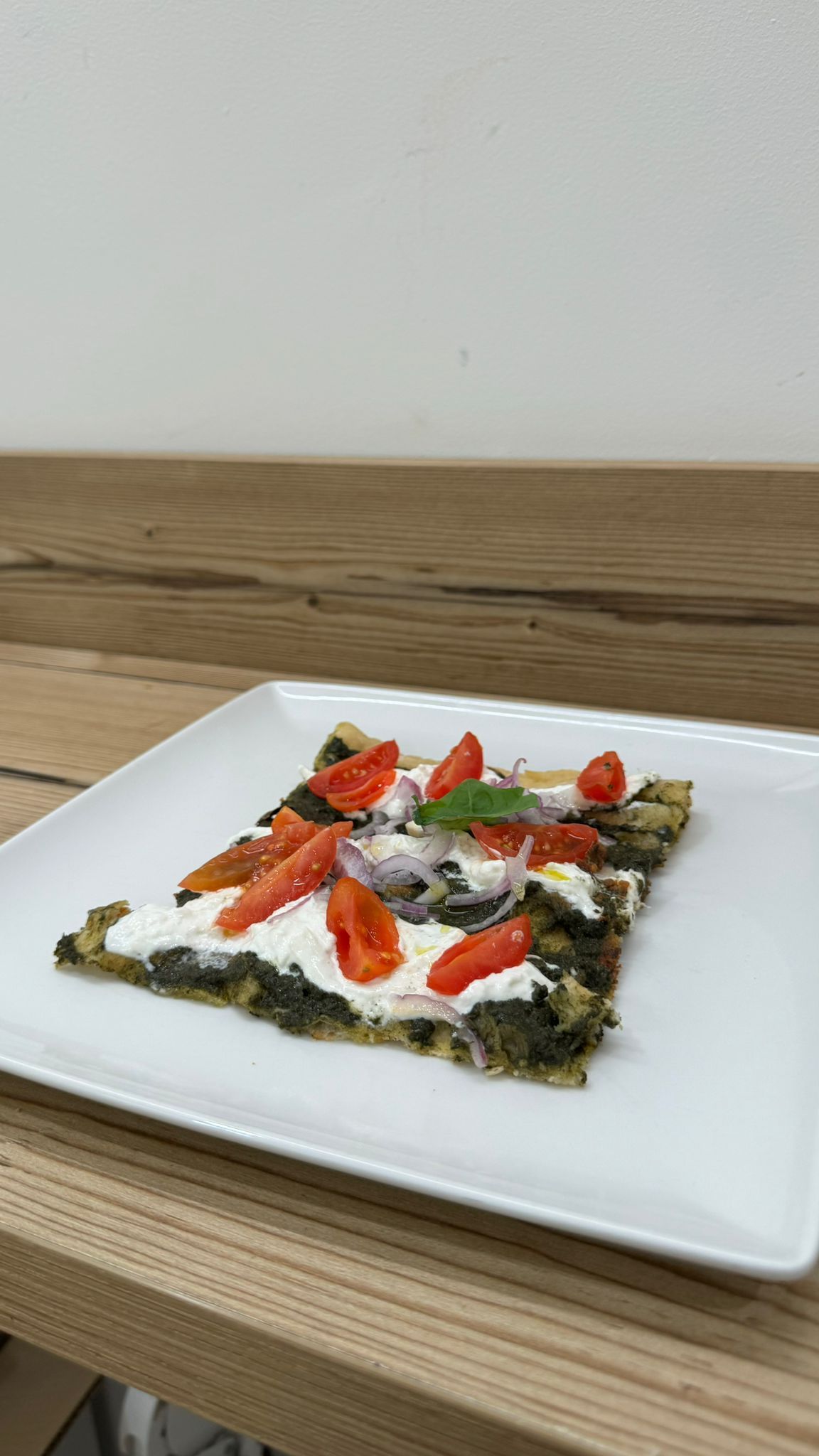 Una fetta di pizza su un piatto bianco su un tavolo di legno.