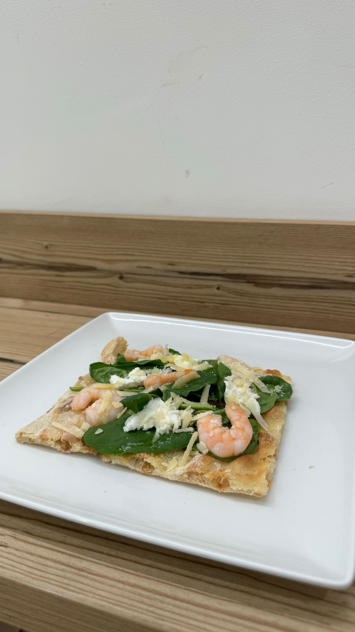 Un piatto bianco sormontato da una fetta di pizza con gamberi e spinaci.