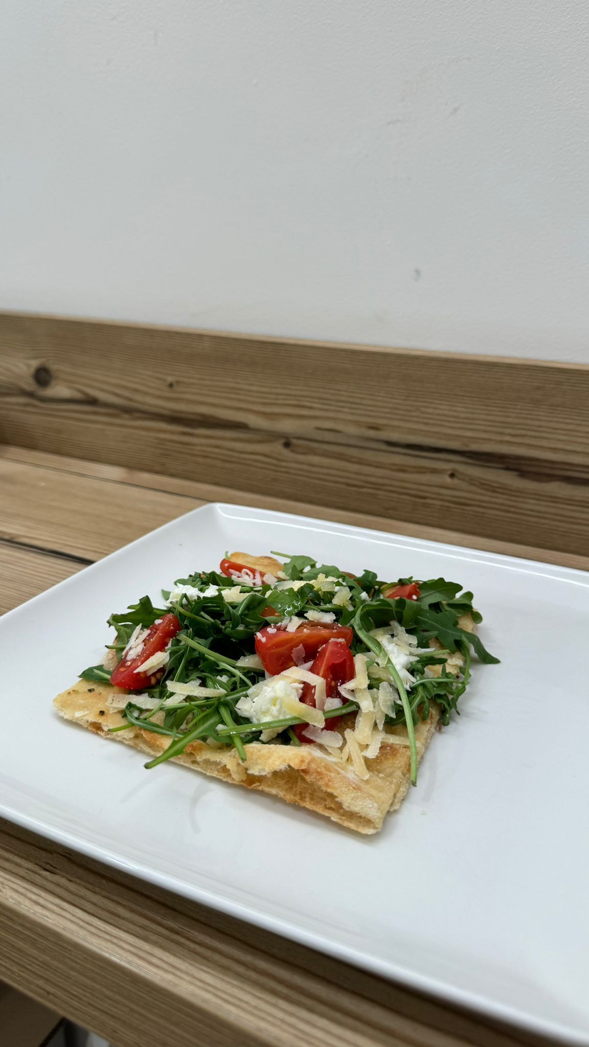 Una fetta di pizza su un piatto bianco su un tavolo di legno.