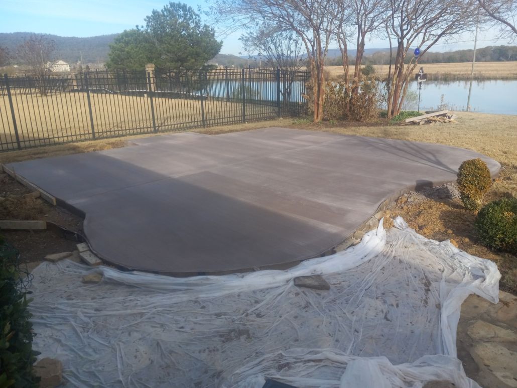 A concrete patio is being built in a backyard next to a lake.