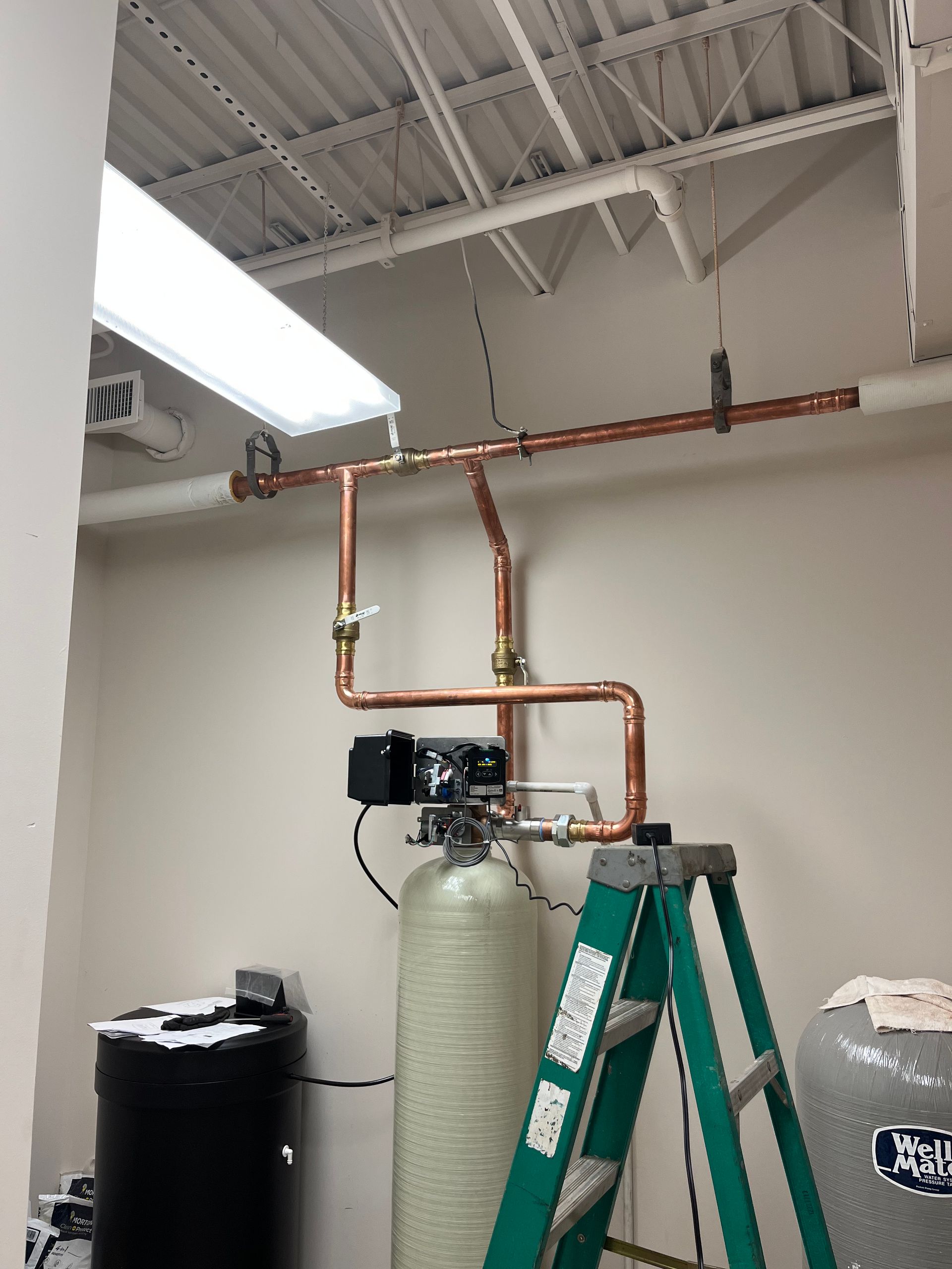 A green ladder is sitting next to a copper pipe in a room.