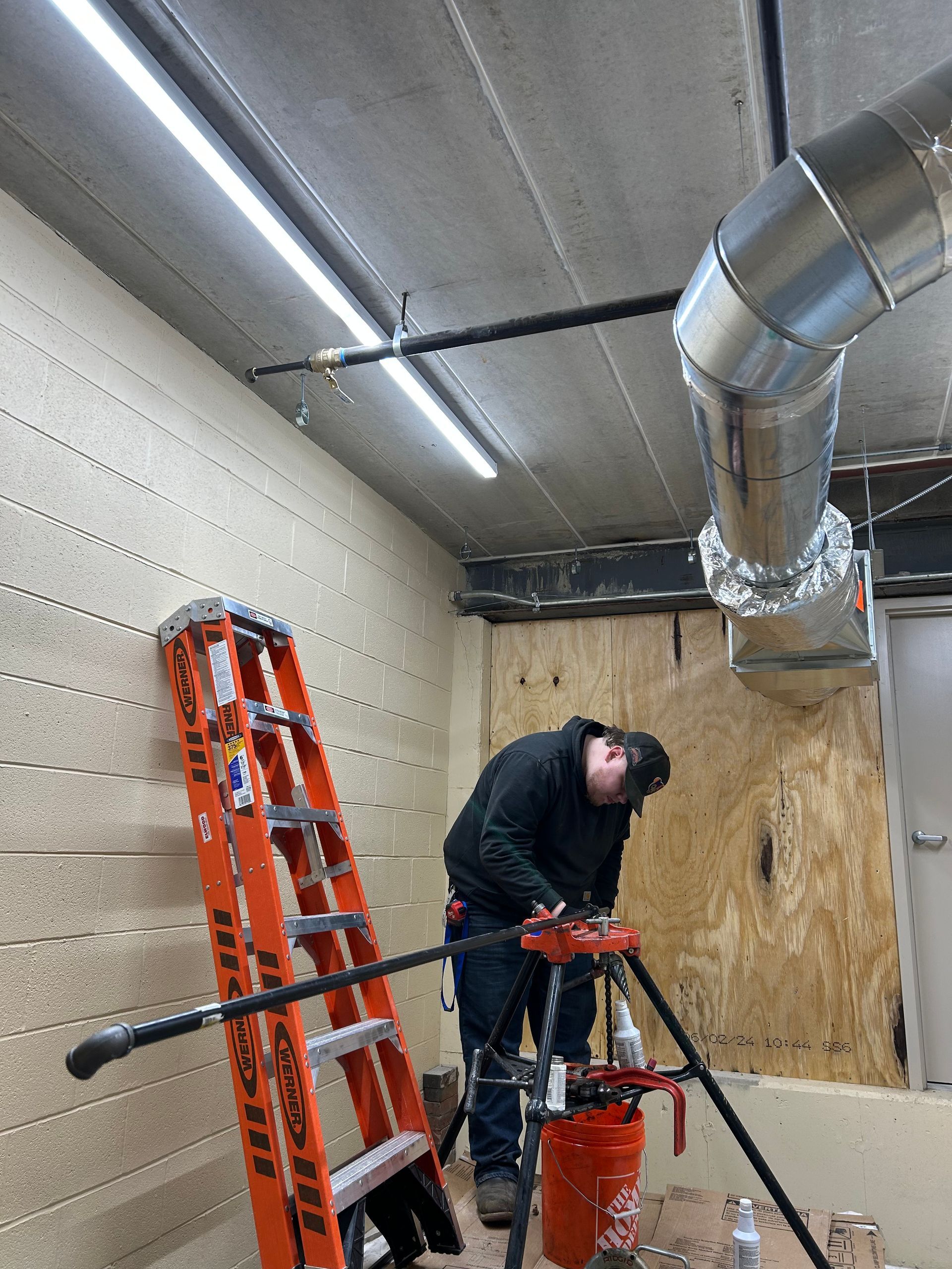 A man is working on a pipe in a room with a ladder.
