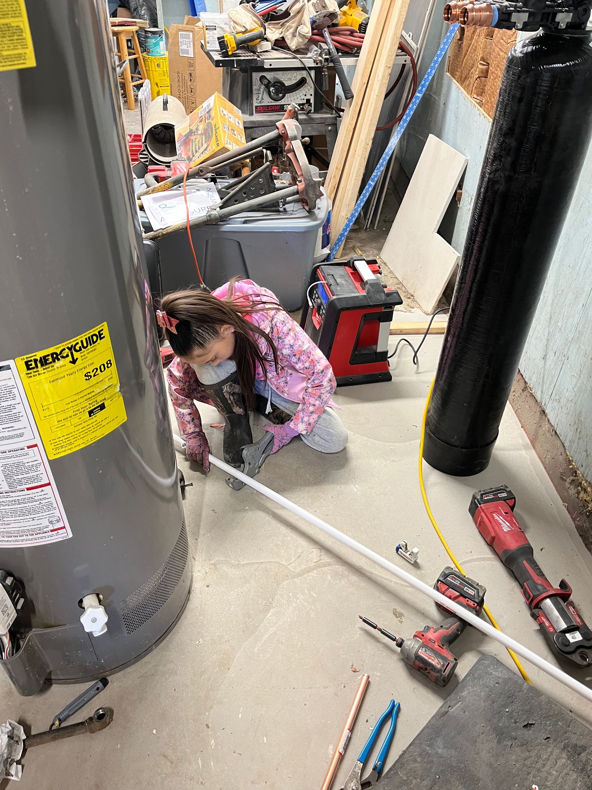 A young girl is working on a water heater in a messy room.