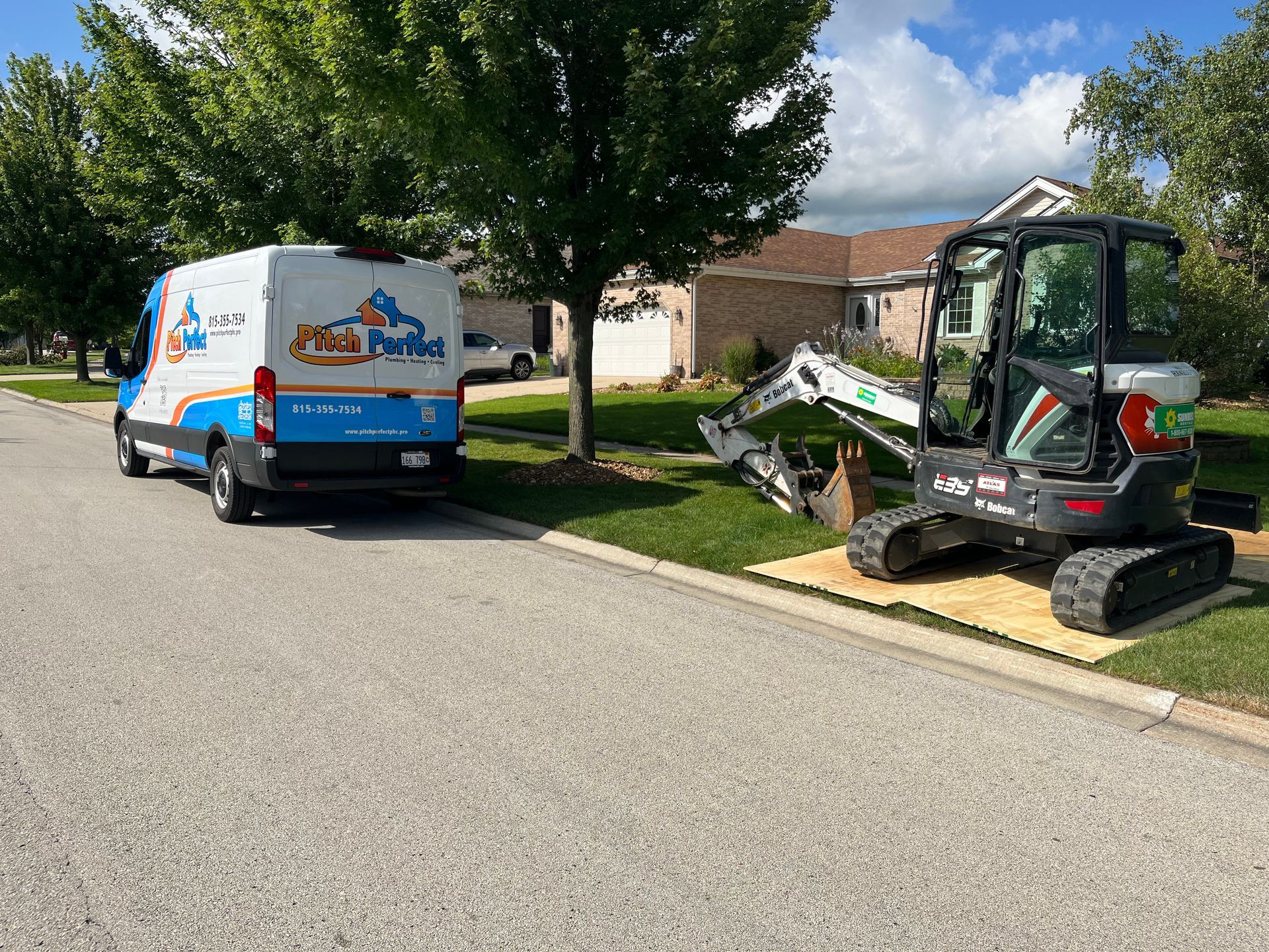 A van is parked next to a small excavator on the side of the road.