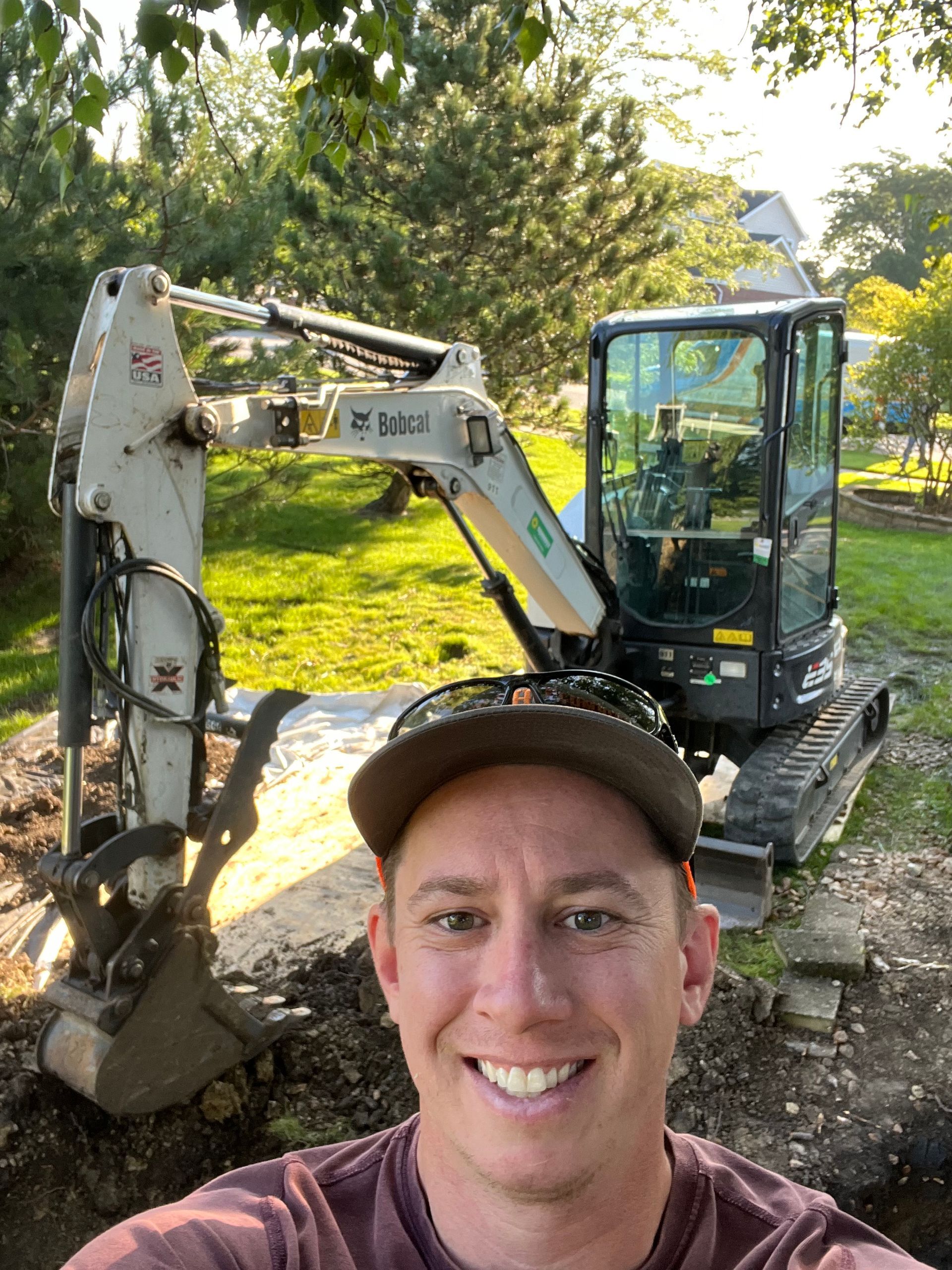 A man is taking a selfie in front of an excavator.