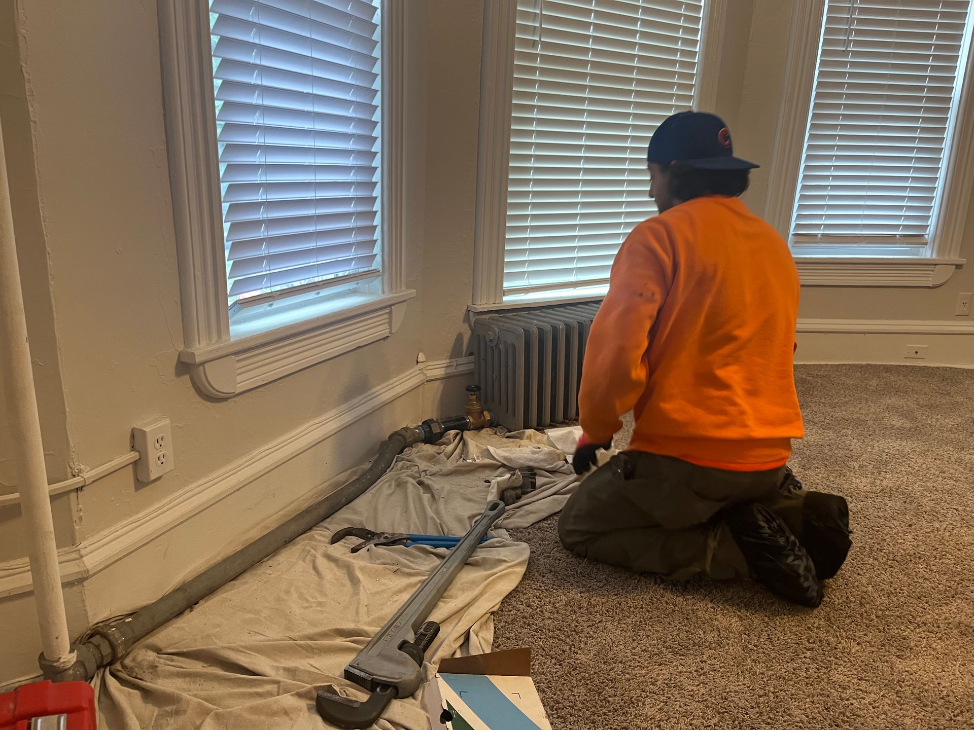 A man is kneeling on the floor in a room fixing a radiator.