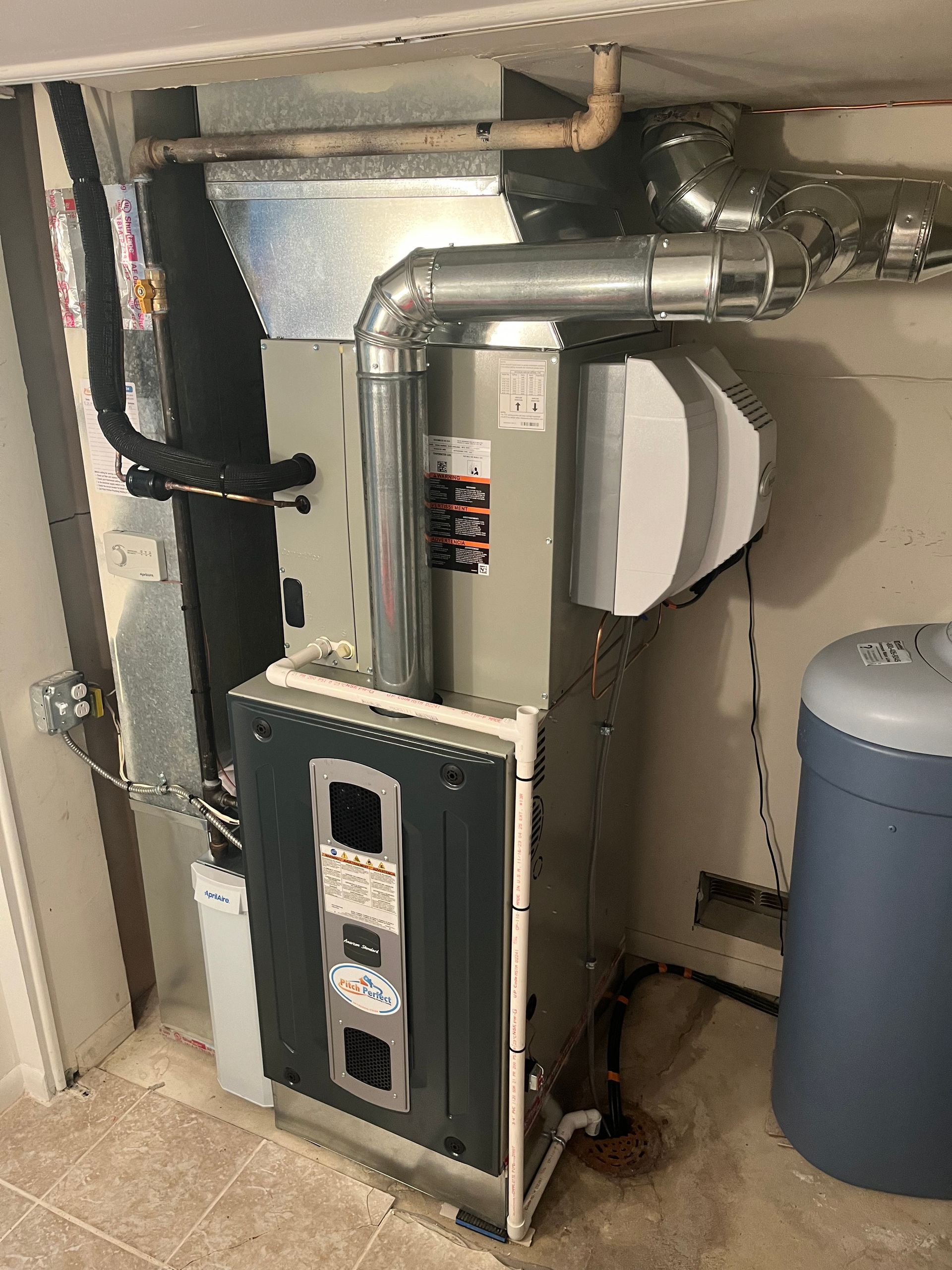 An air conditioner is sitting in a basement next to a blue tank.