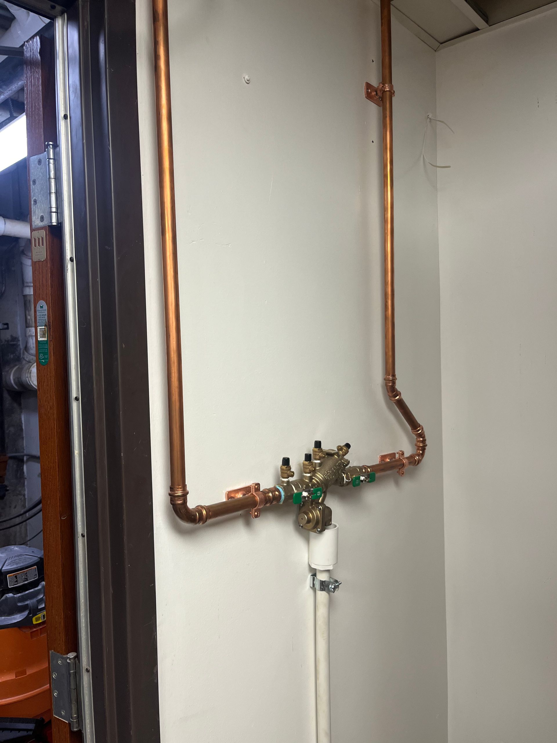 A copper pipe is hanging on a white wall next to a door.