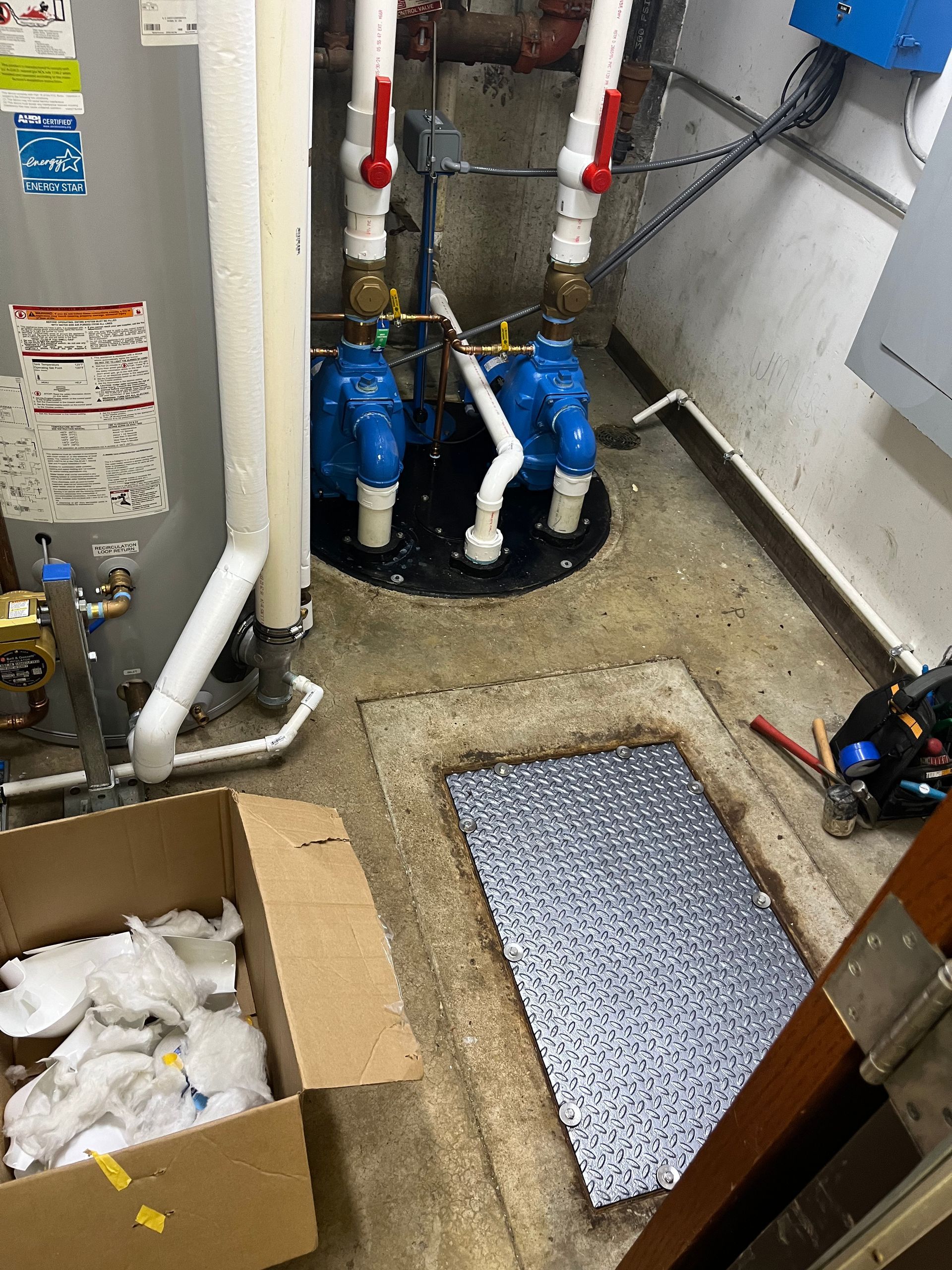 A room with a water heater , pipes , and a box on the floor.