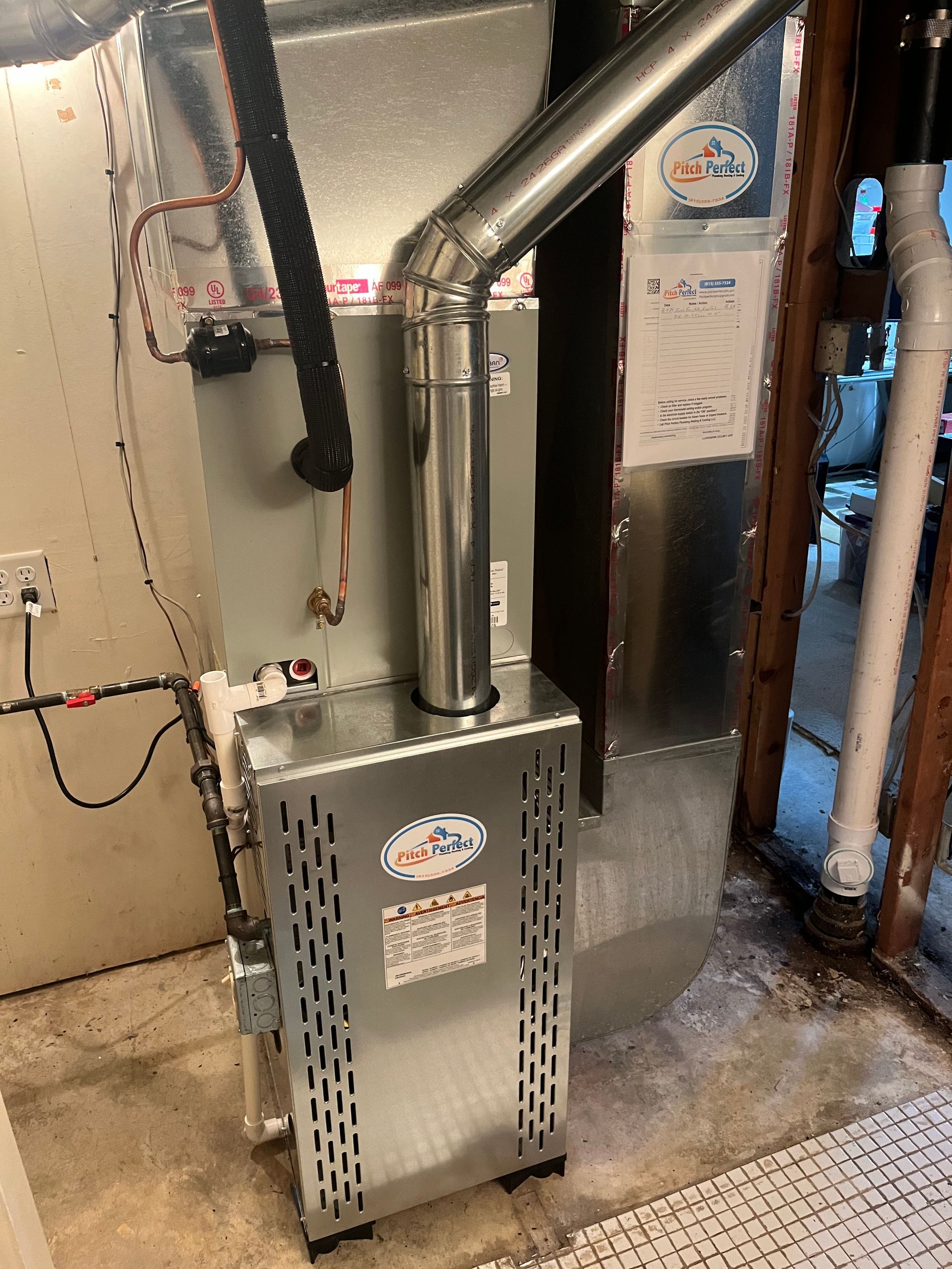 A stainless steel furnace is sitting in a basement next to a door.