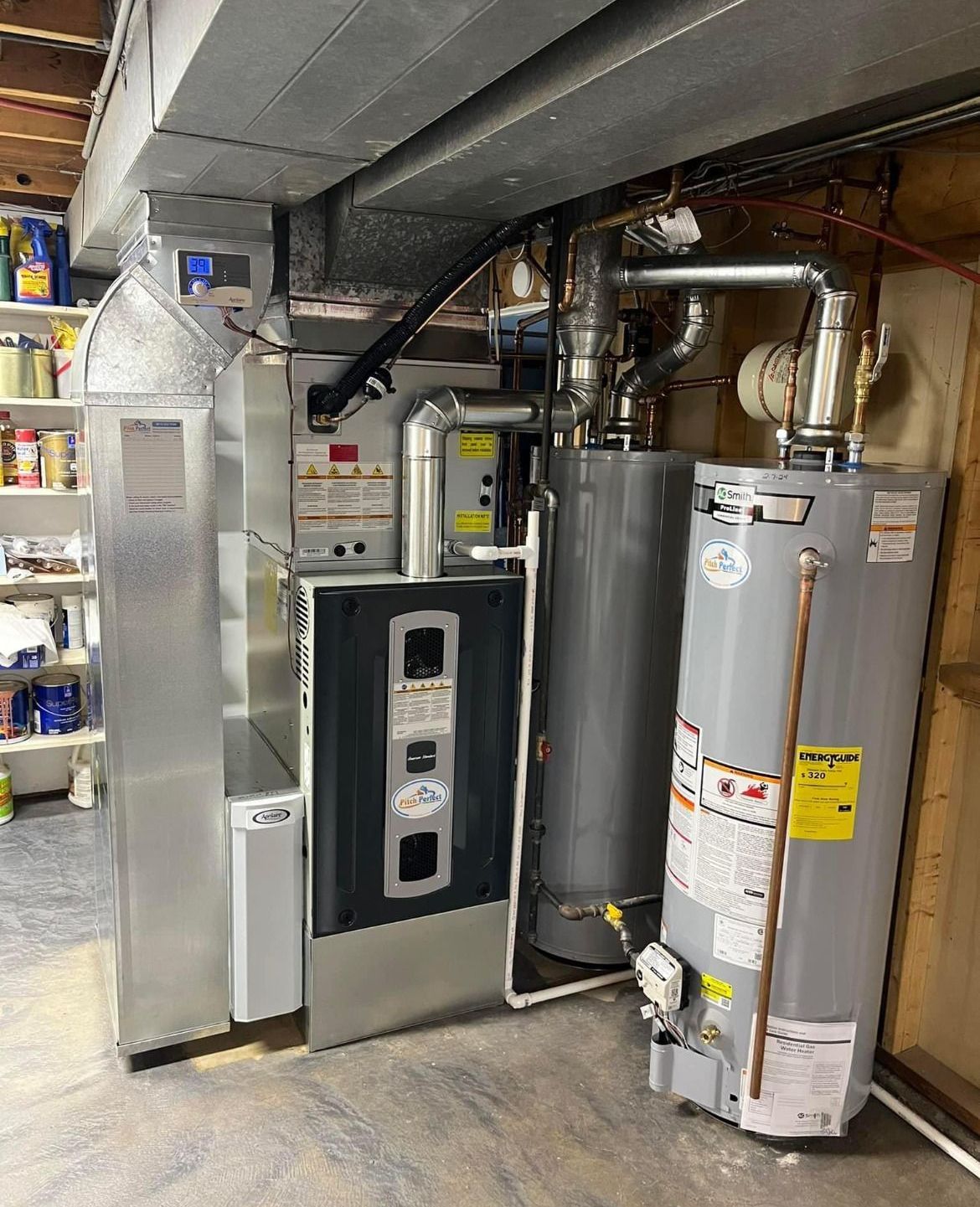Furnace, water heaters, and ductwork in a basement. Silver appliances against a light gray concrete floor.