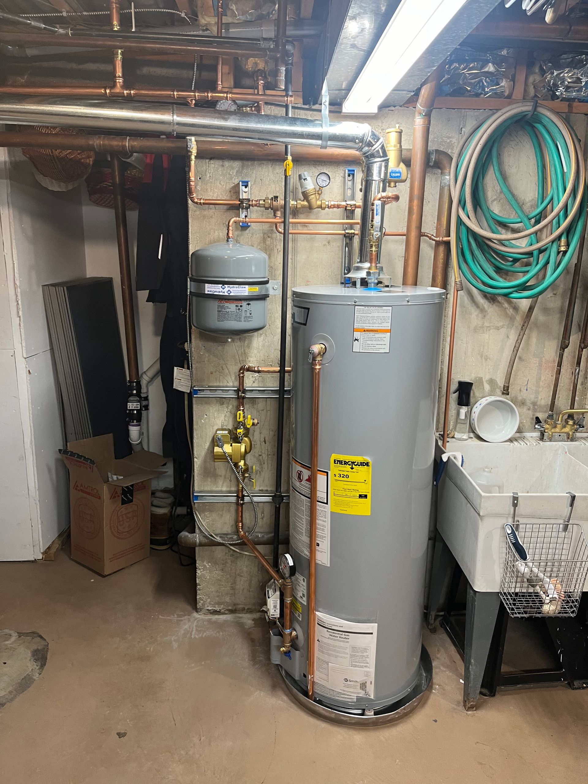 A water heater is sitting in a basement next to a sink.