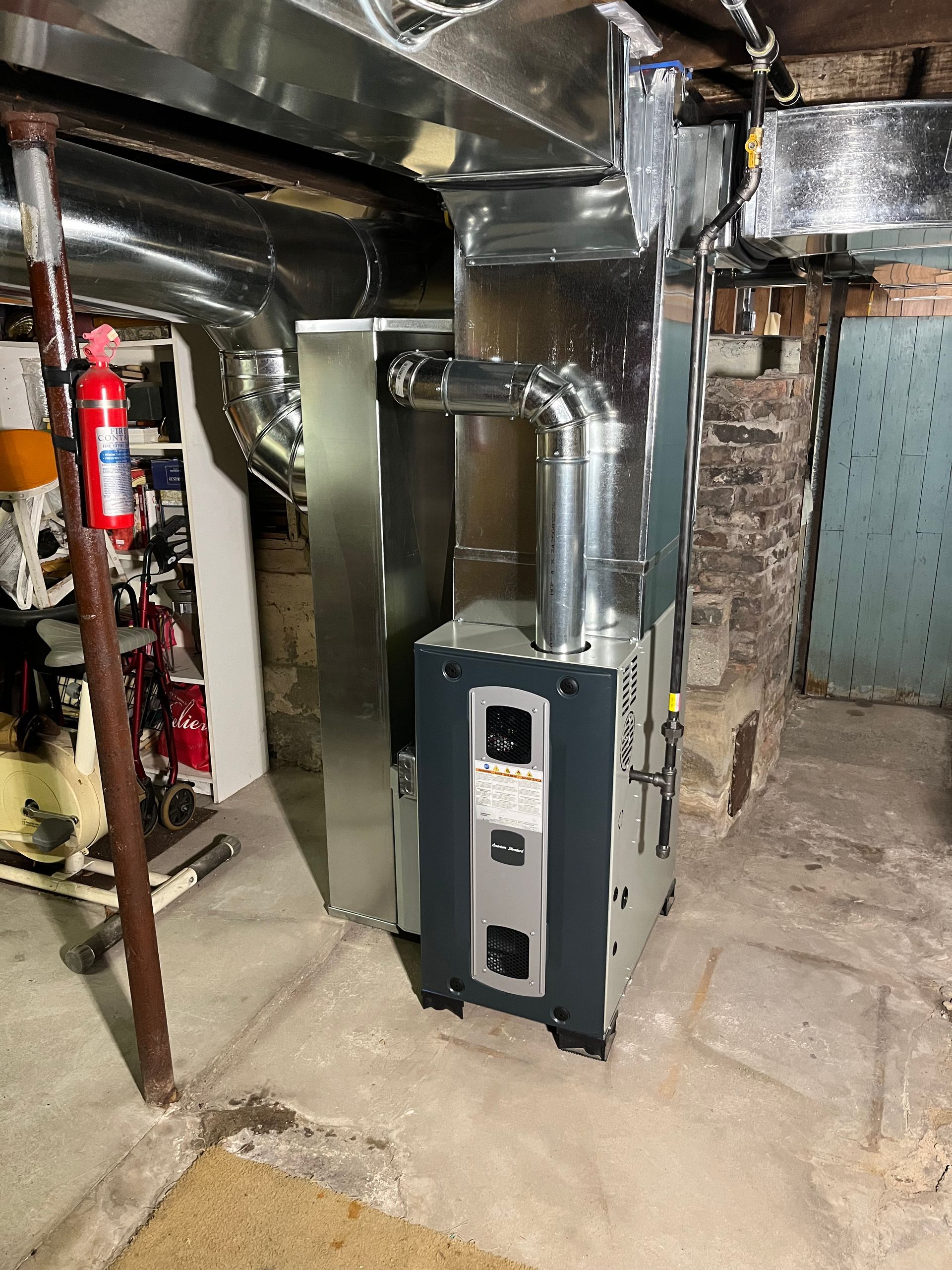 Furnace in a basement with silver ductwork and a fire extinguisher nearby.