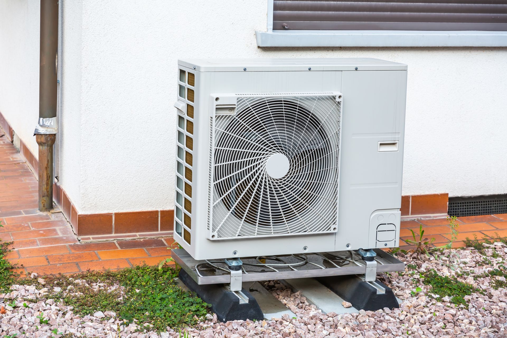 Outdoor air conditioning unit, gray with fan, sits on a platform next to a building.