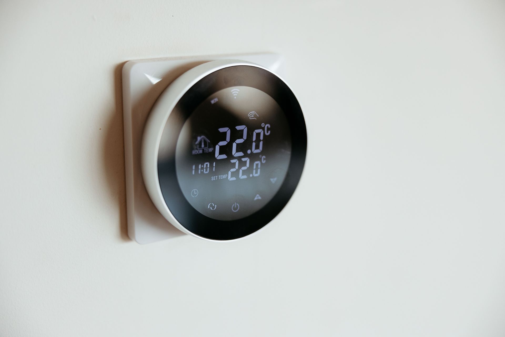 A round, smart thermostat on a white wall displays 22.0°C, with a black screen and white frame.