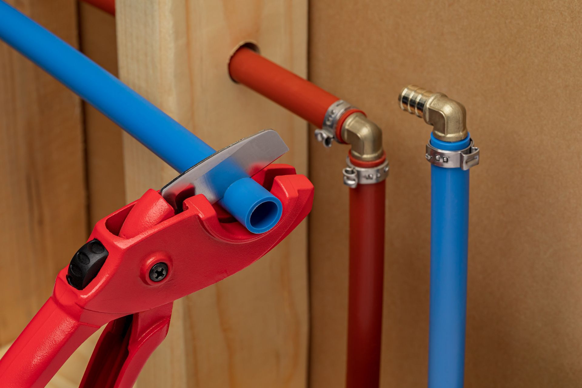 Red pipe cutter slicing blue PEX pipe near red and blue pipes with brass fittings.