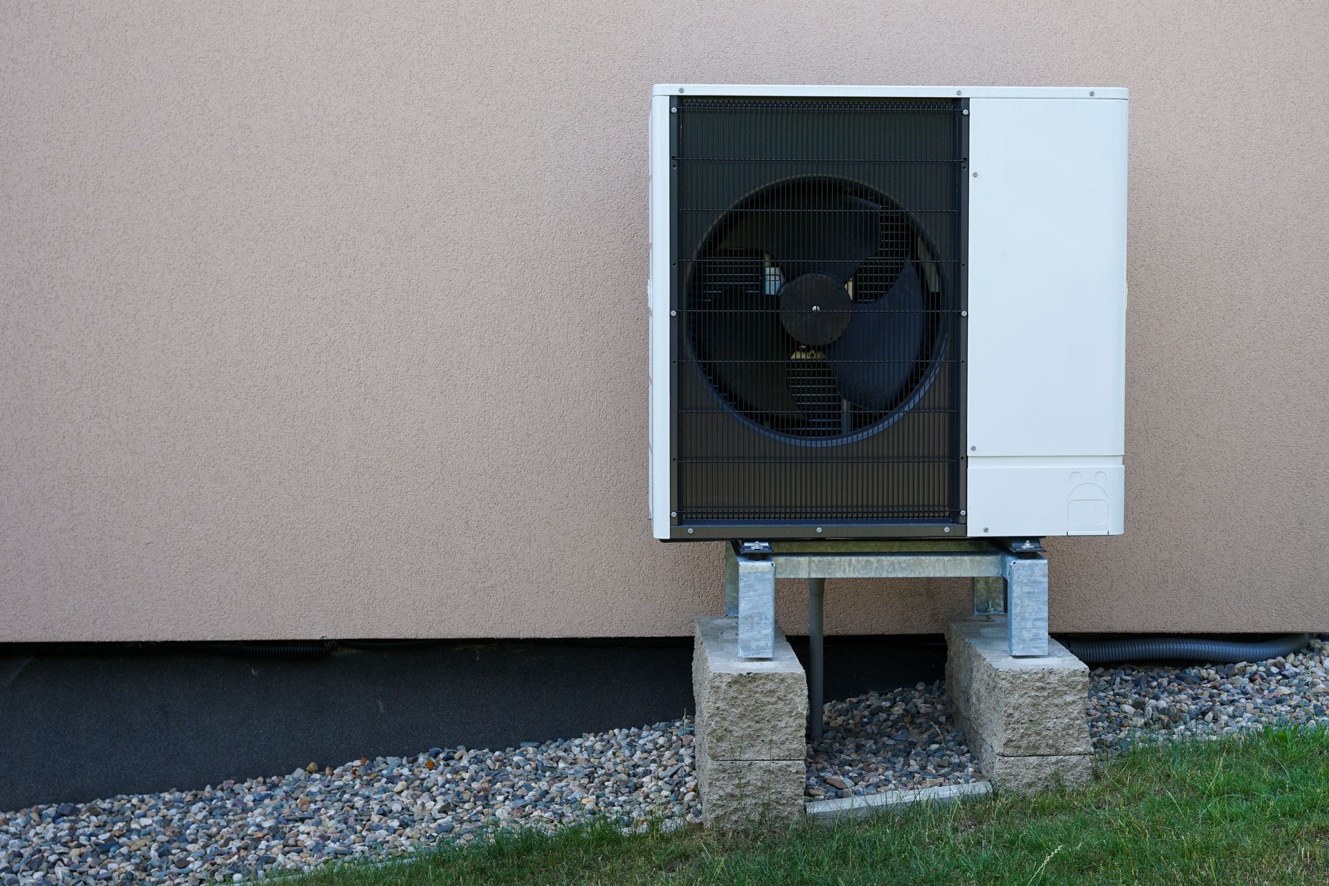 Air conditioner unit on concrete blocks, against a beige wall and gravel.