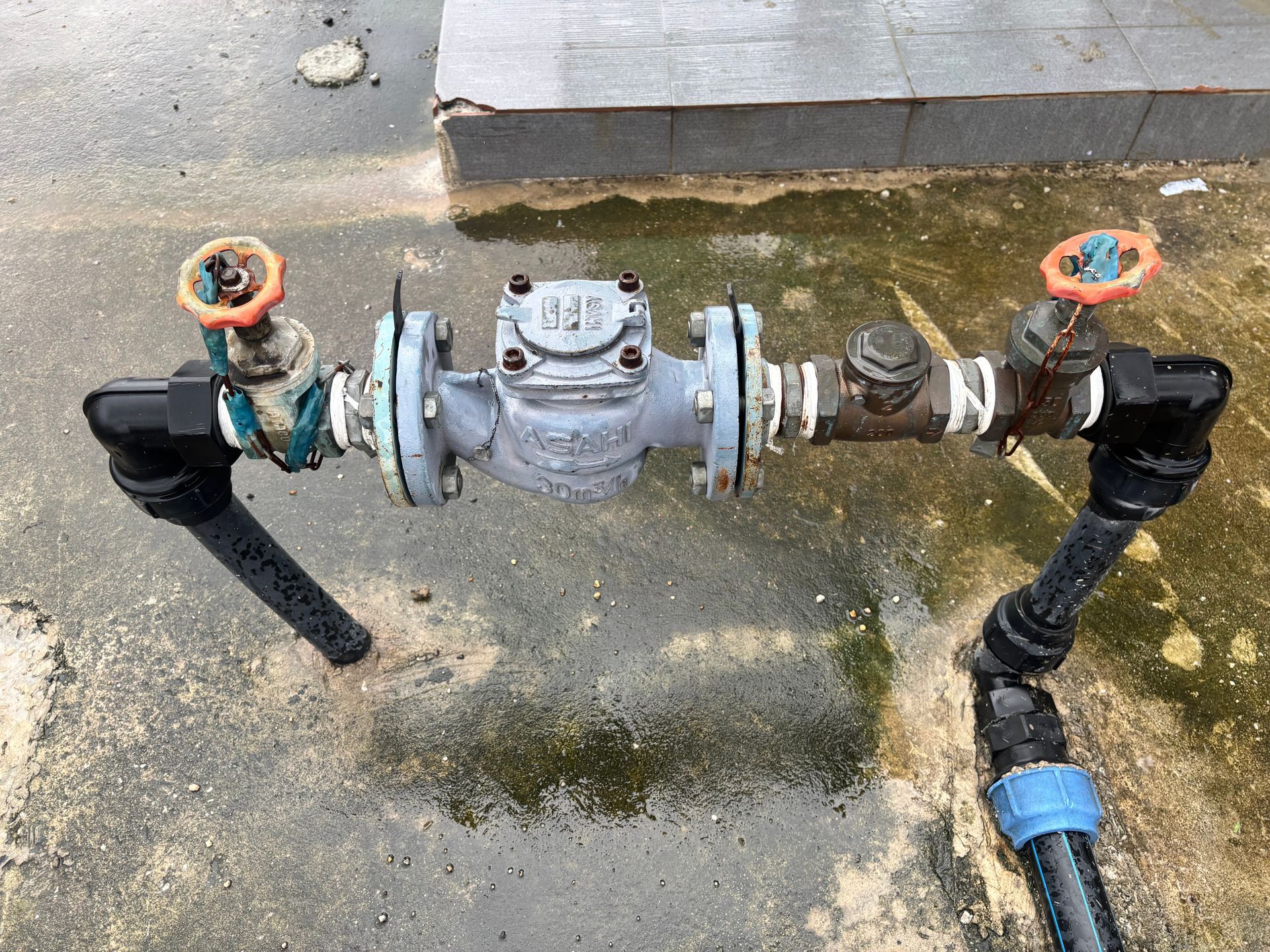 Water pipes with valves and a meter on a wet concrete surface.