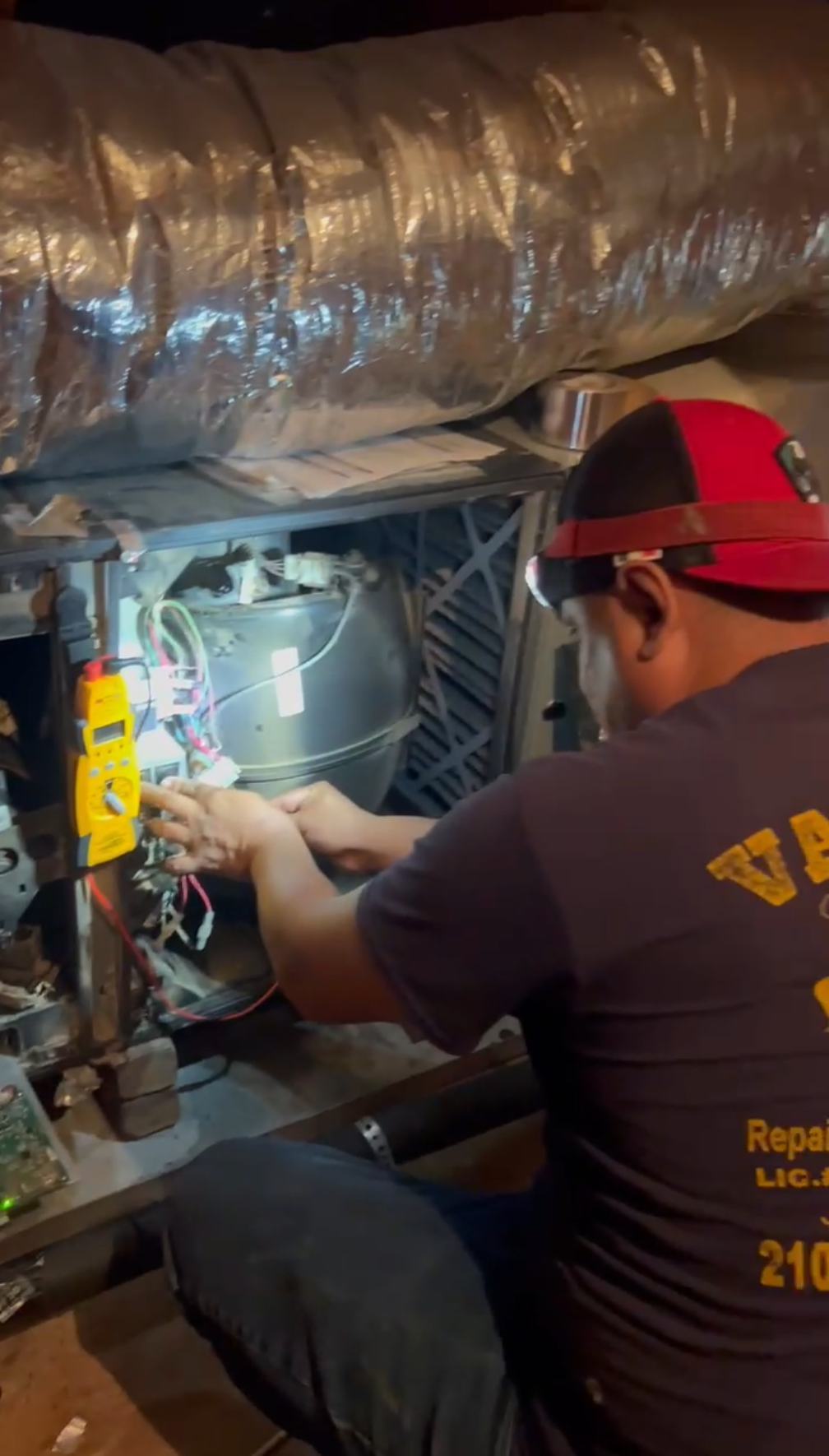 HVAC technician repairs furnace, uses tools and headlamp in crawlspace.