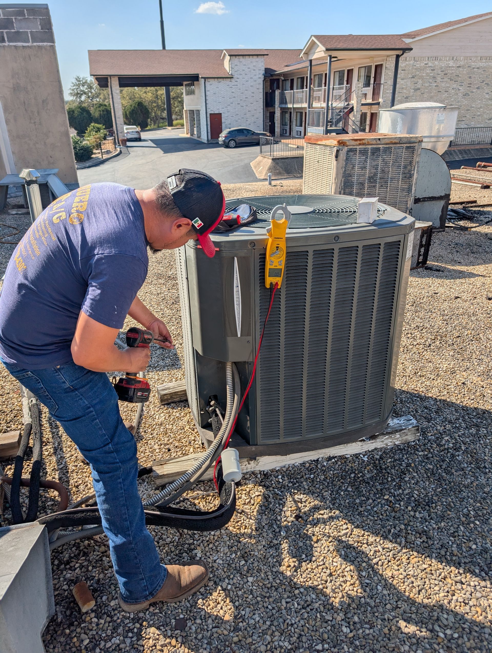 HVAC technician in yellow vest and hard hat repairs an air conditioning unit on a rooftop.