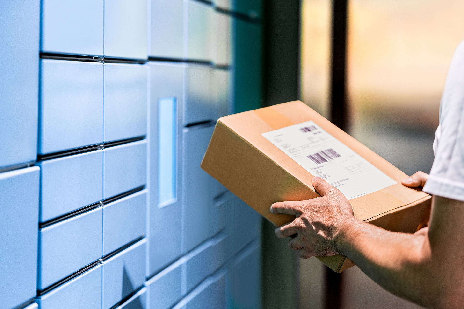 A person is holding a cardboard box in front of a locker.