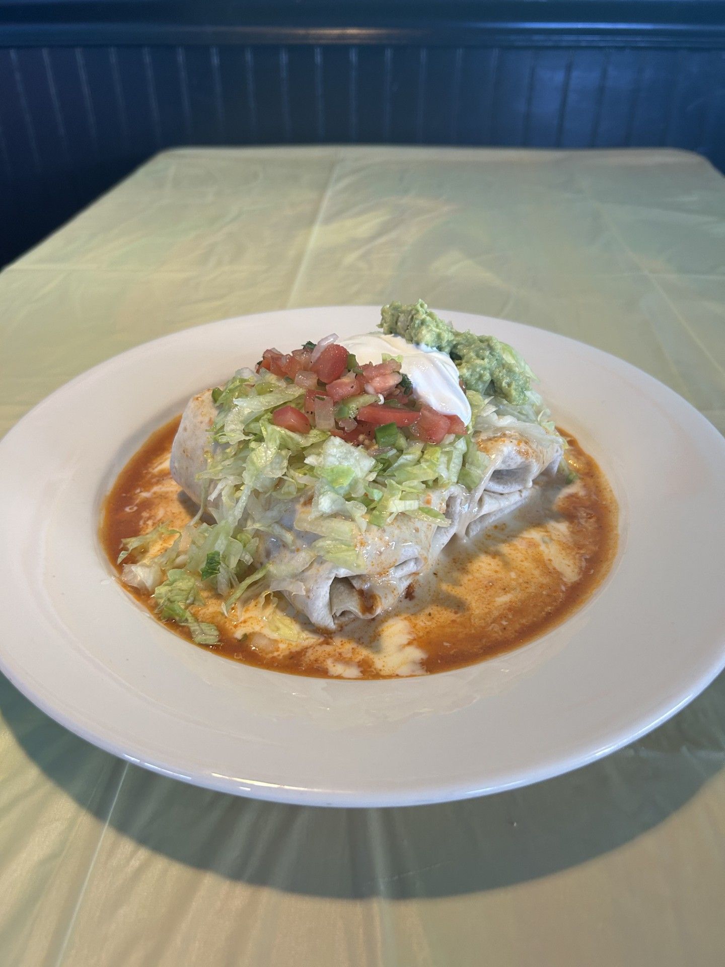 A burrito is sitting on a white plate on a table.