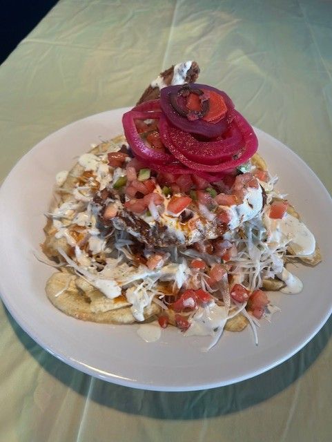 Plate of loaded food: flatbread with toppings, including pickled onions, tomatoes, and sauce.