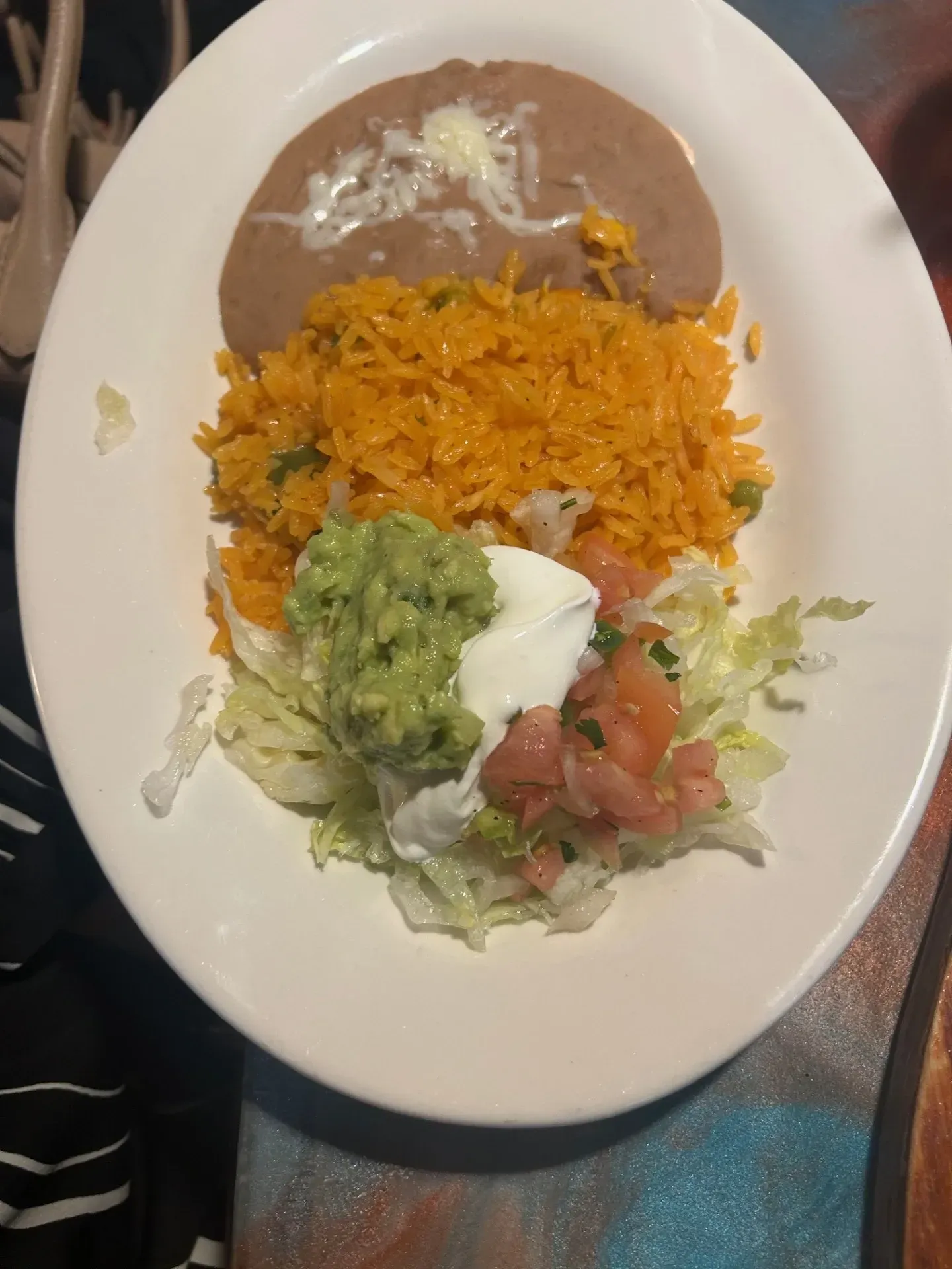 A white plate topped with rice beans guacamole and lettuce.