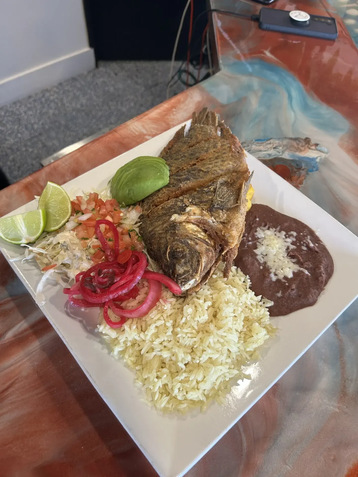 A white plate topped with rice , beans , and a fish on a table.