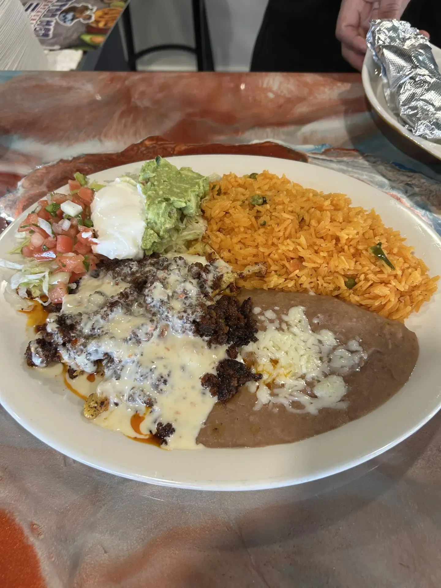 A plate of mexican food with rice , beans , guacamole and cheese on a table.