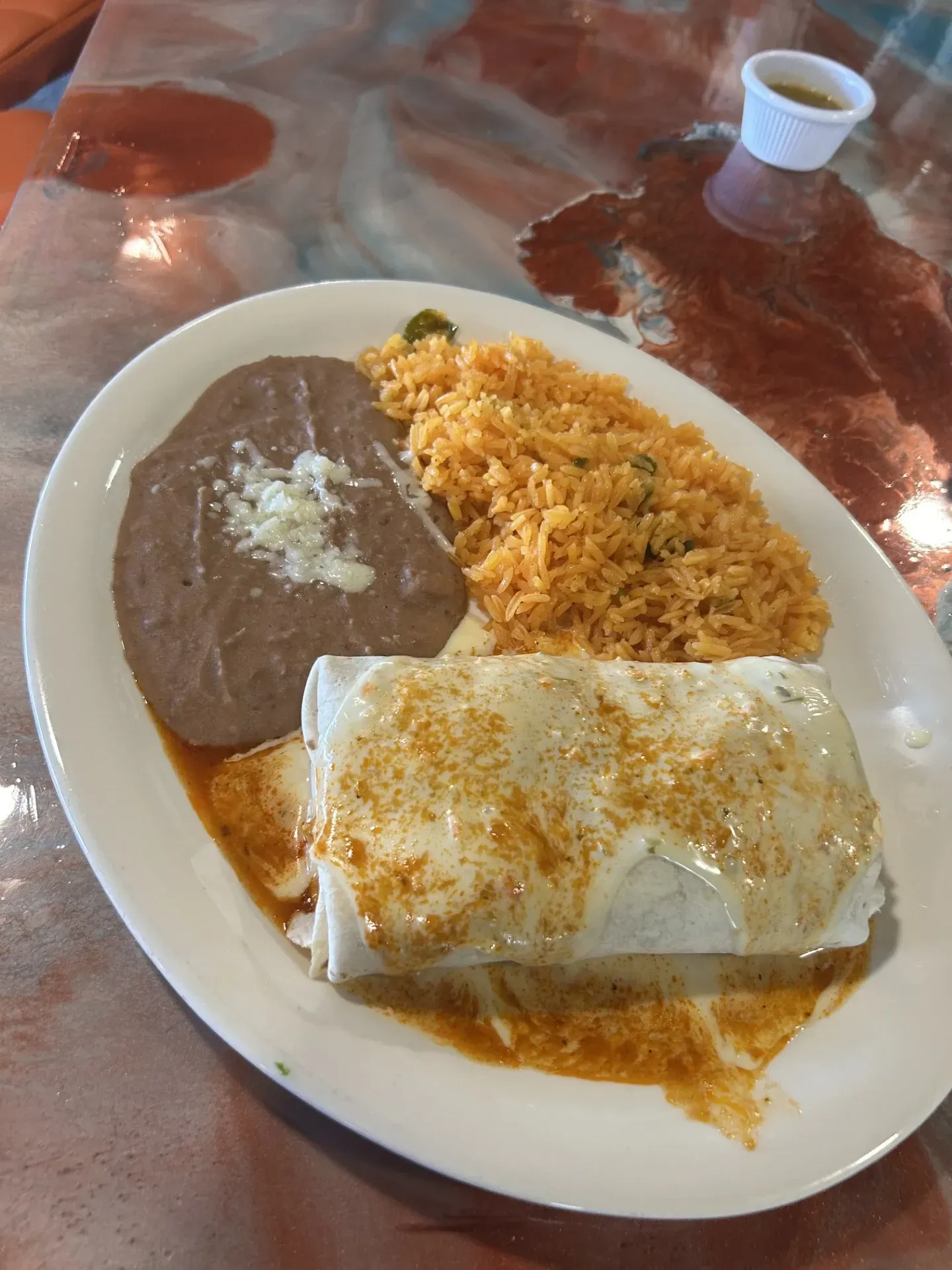 A white plate topped with a burrito , rice and beans on a table.