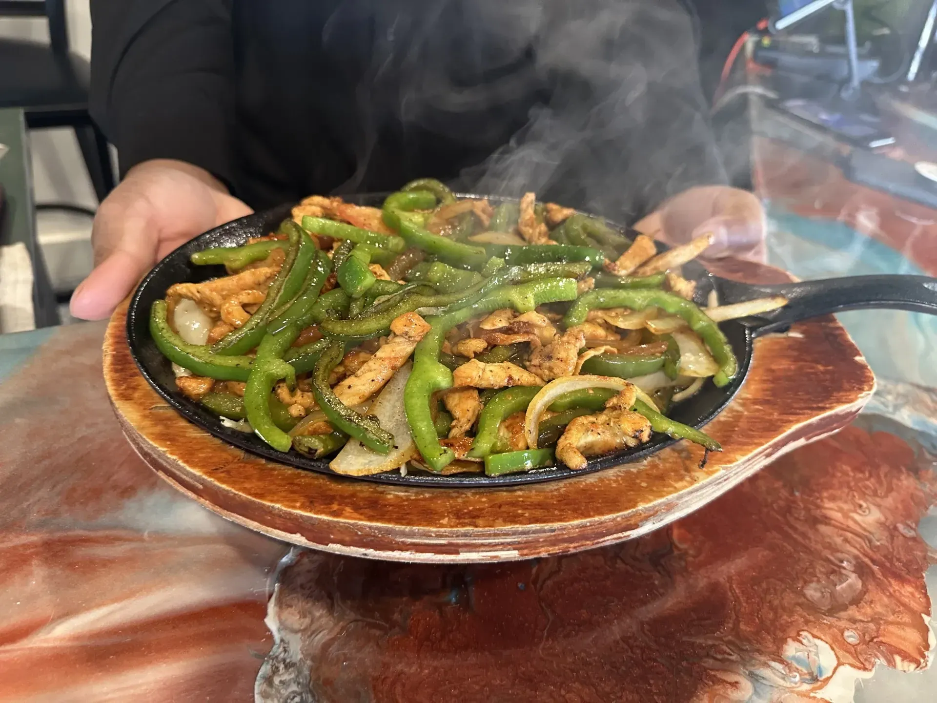 A person is holding a pan of food with green peppers and chicken.