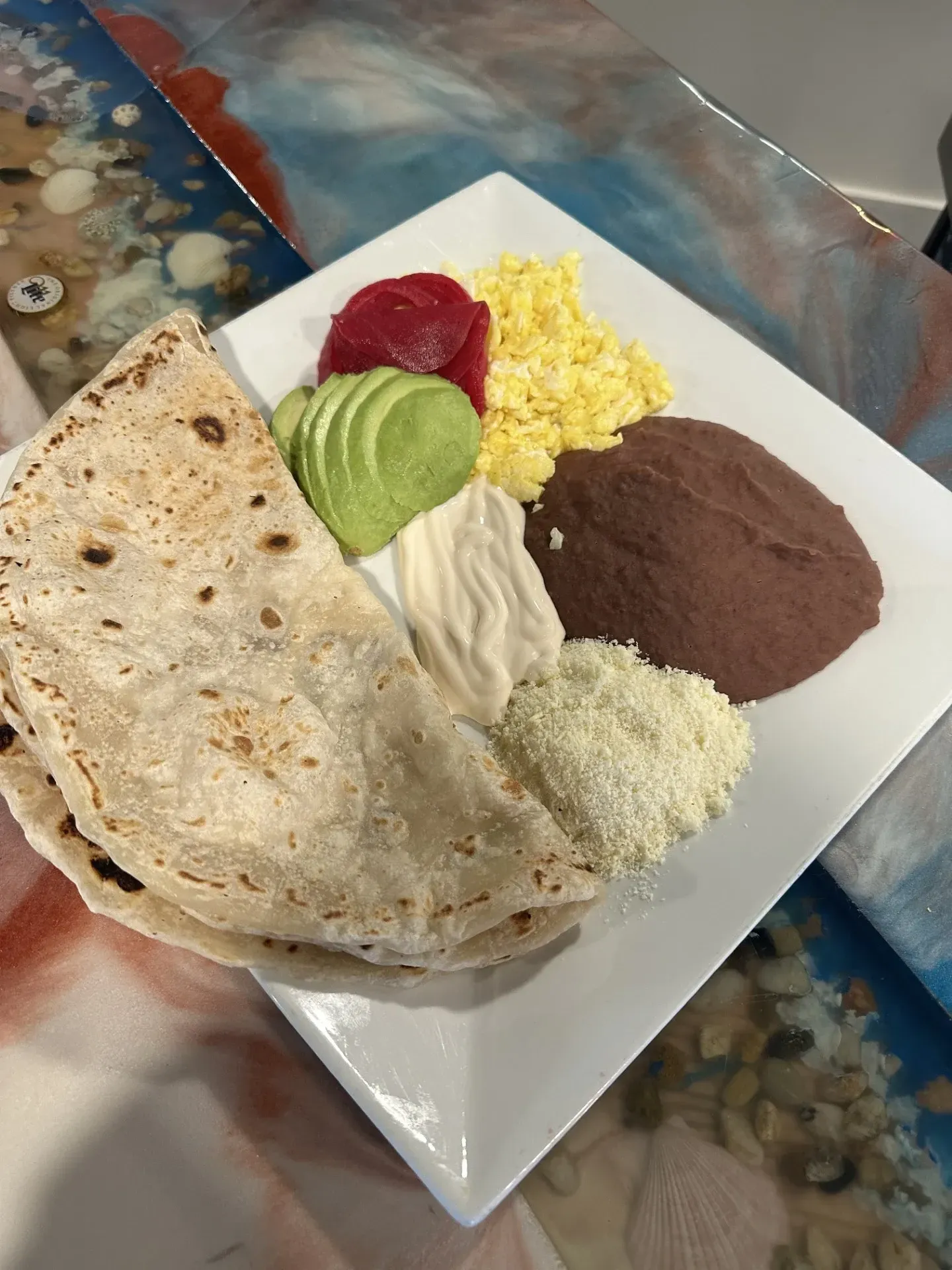 A white plate topped with a tortilla , eggs , avocado , and beans.