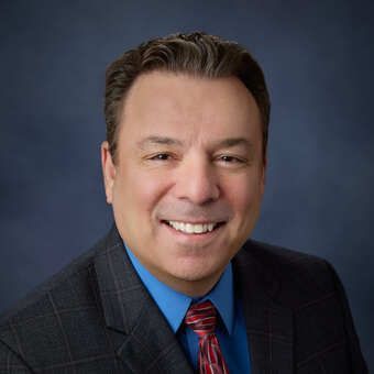 A man is holding a dog in his arms and the dog is wearing a sweater.