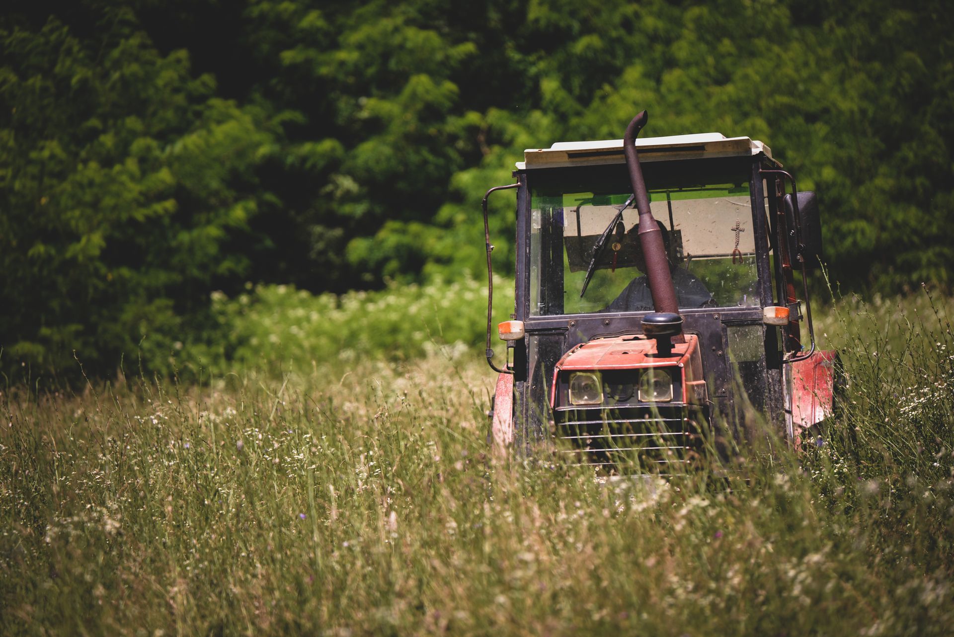A red tractor is driving through a grassy field.