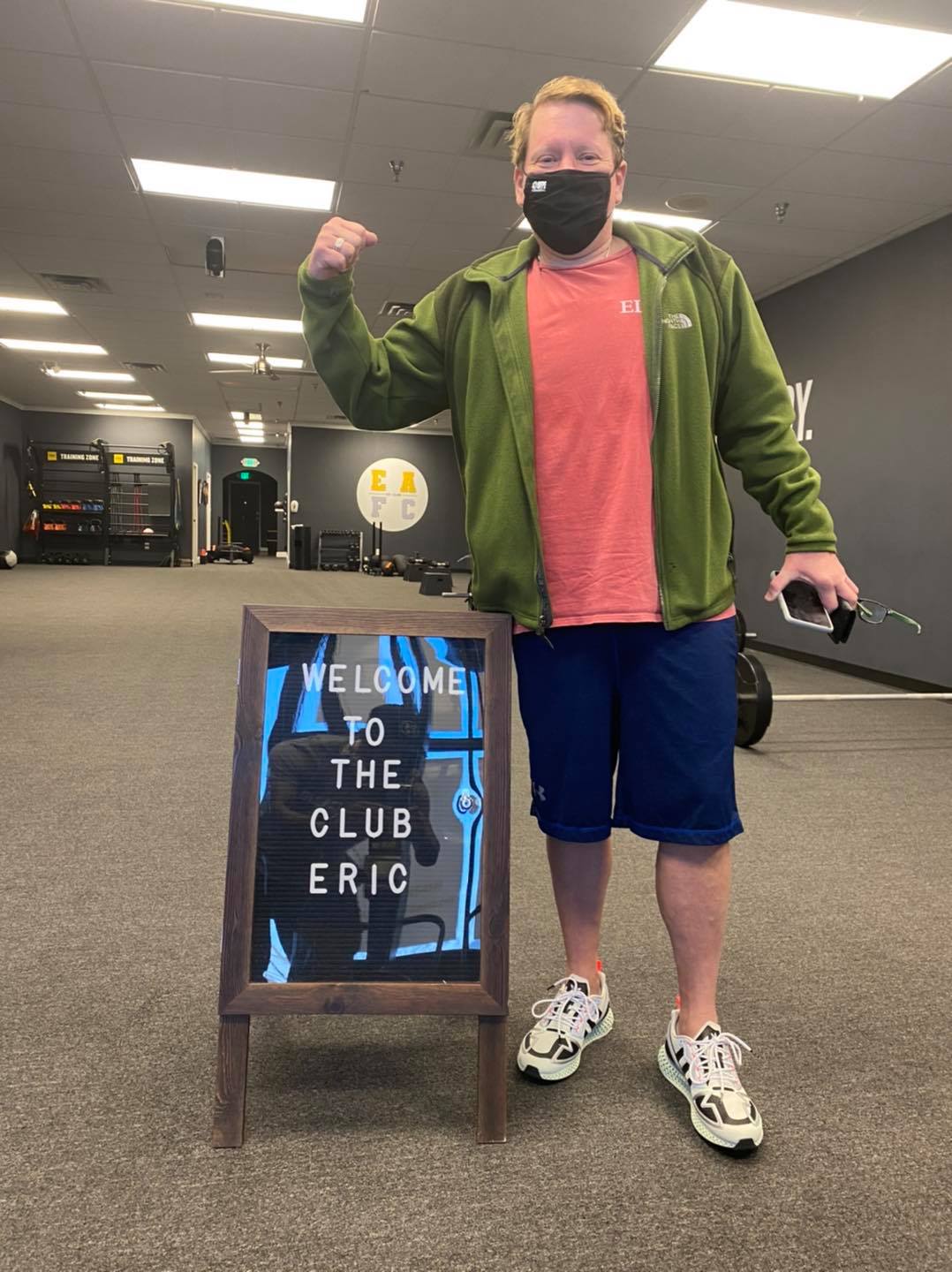 a man wearing a mask is standing in front of a sign that says welcome to the club eric .
