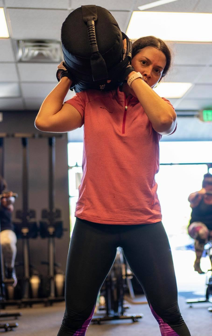 a woman is holding a weight bag over her head in a gym .