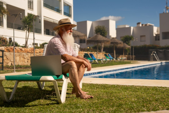 Oudere man die geniet in het buitenland op zijn stoeltje bij het zwembad.