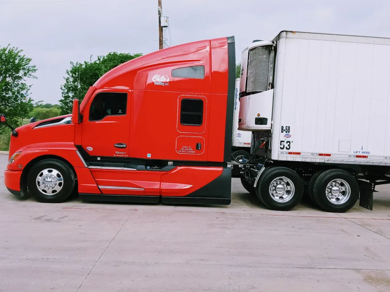 A red semi truck is parked next to a white trailer.